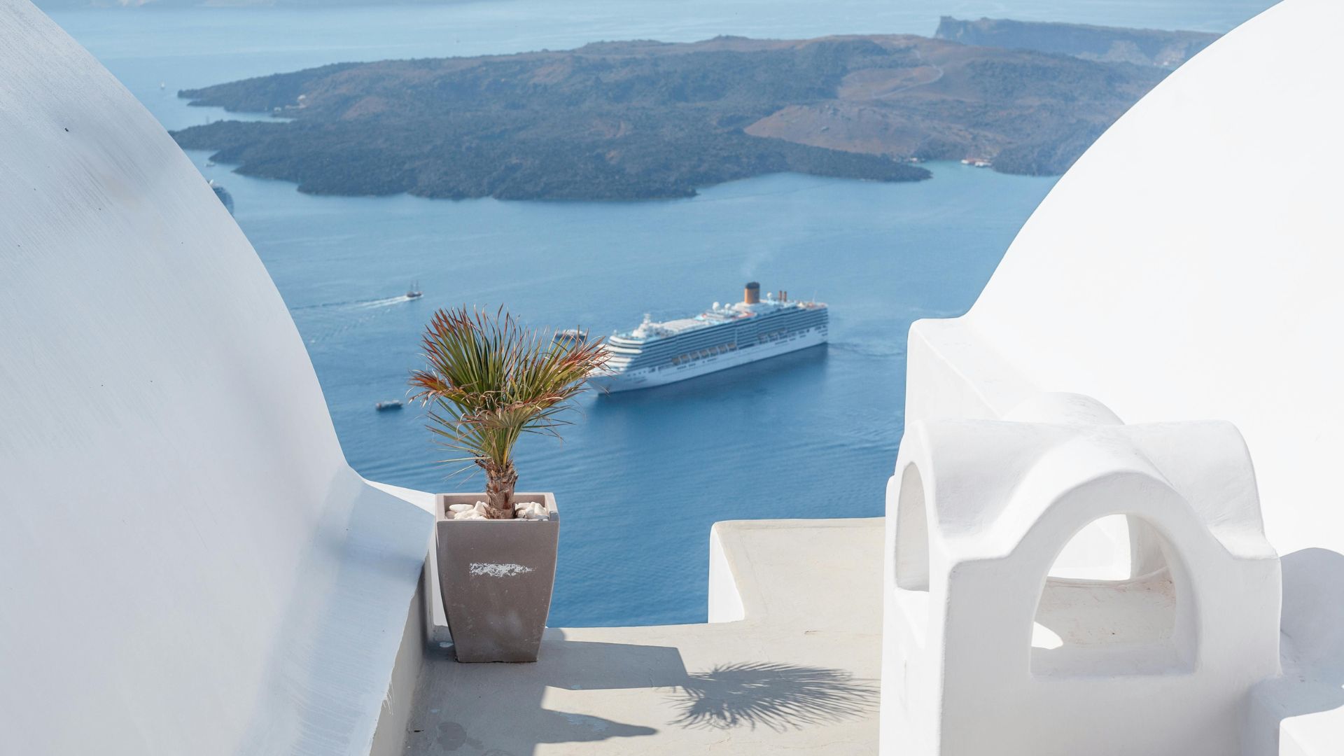 View of the Aegean Sea and a cruise ship from a white-washed building in Santorini.