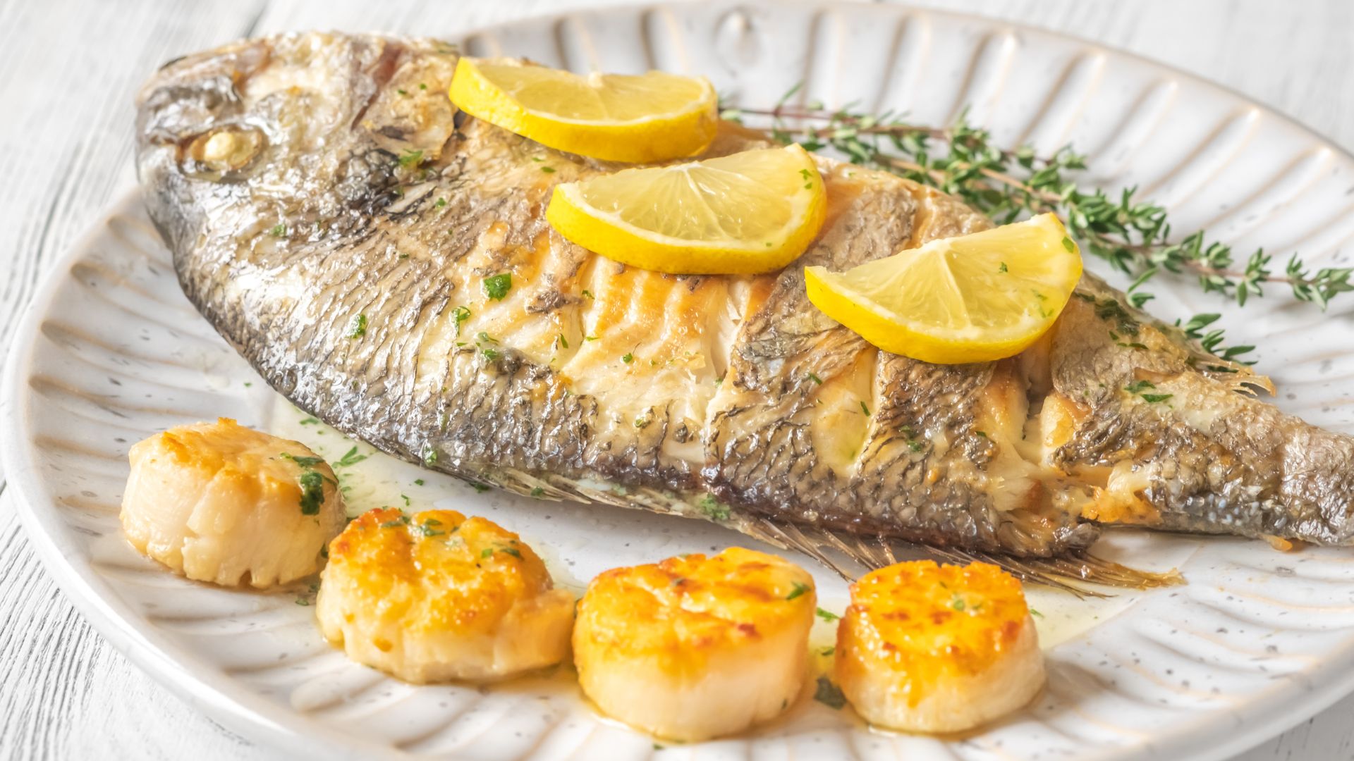 The fresh grilled orata, is garnished with lemon slices and herbs, and accompanied by what appear to be scallops.