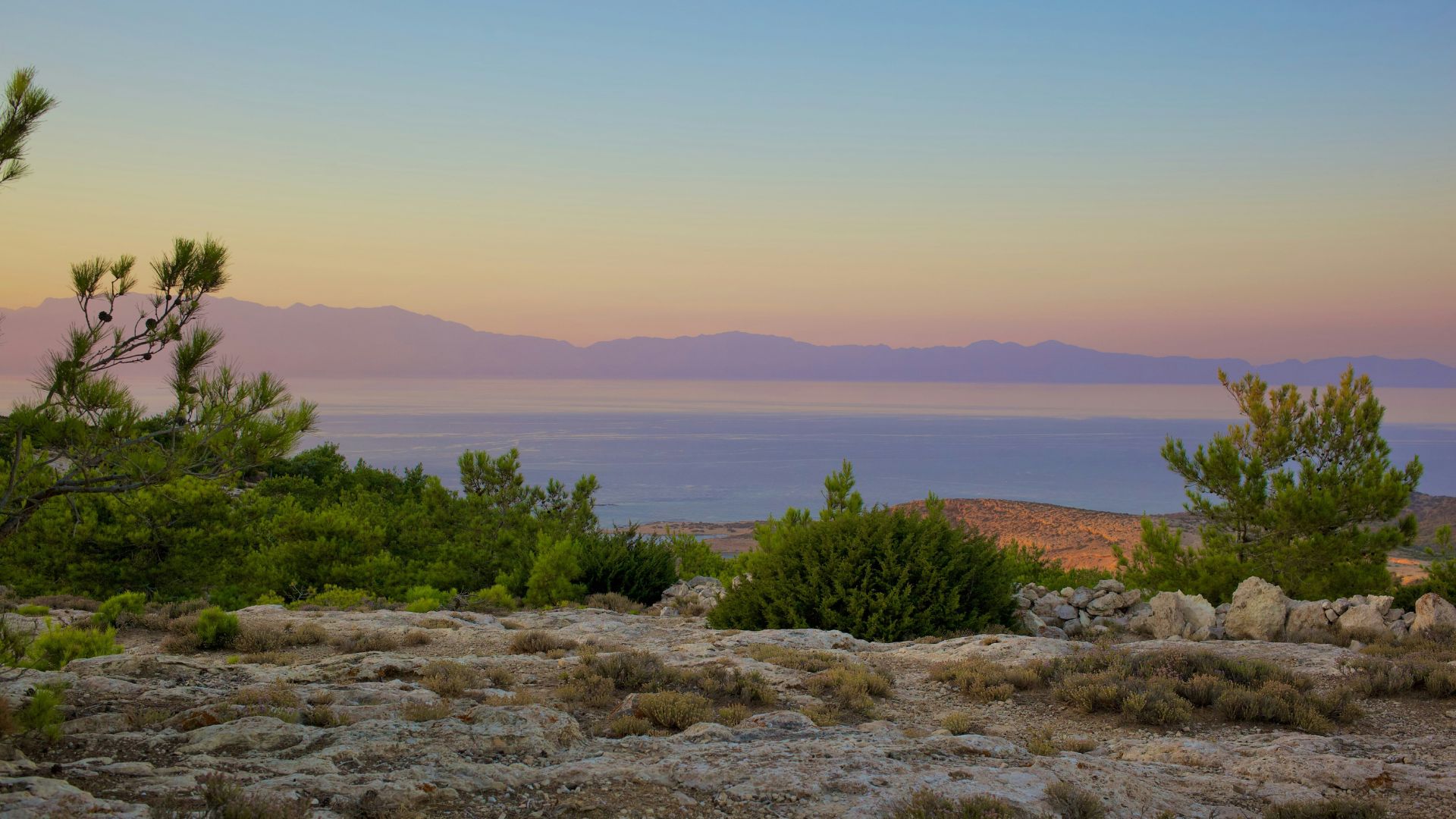 A scenic view of Gavdopoula island at sunset, with the sea and mountains in the background.