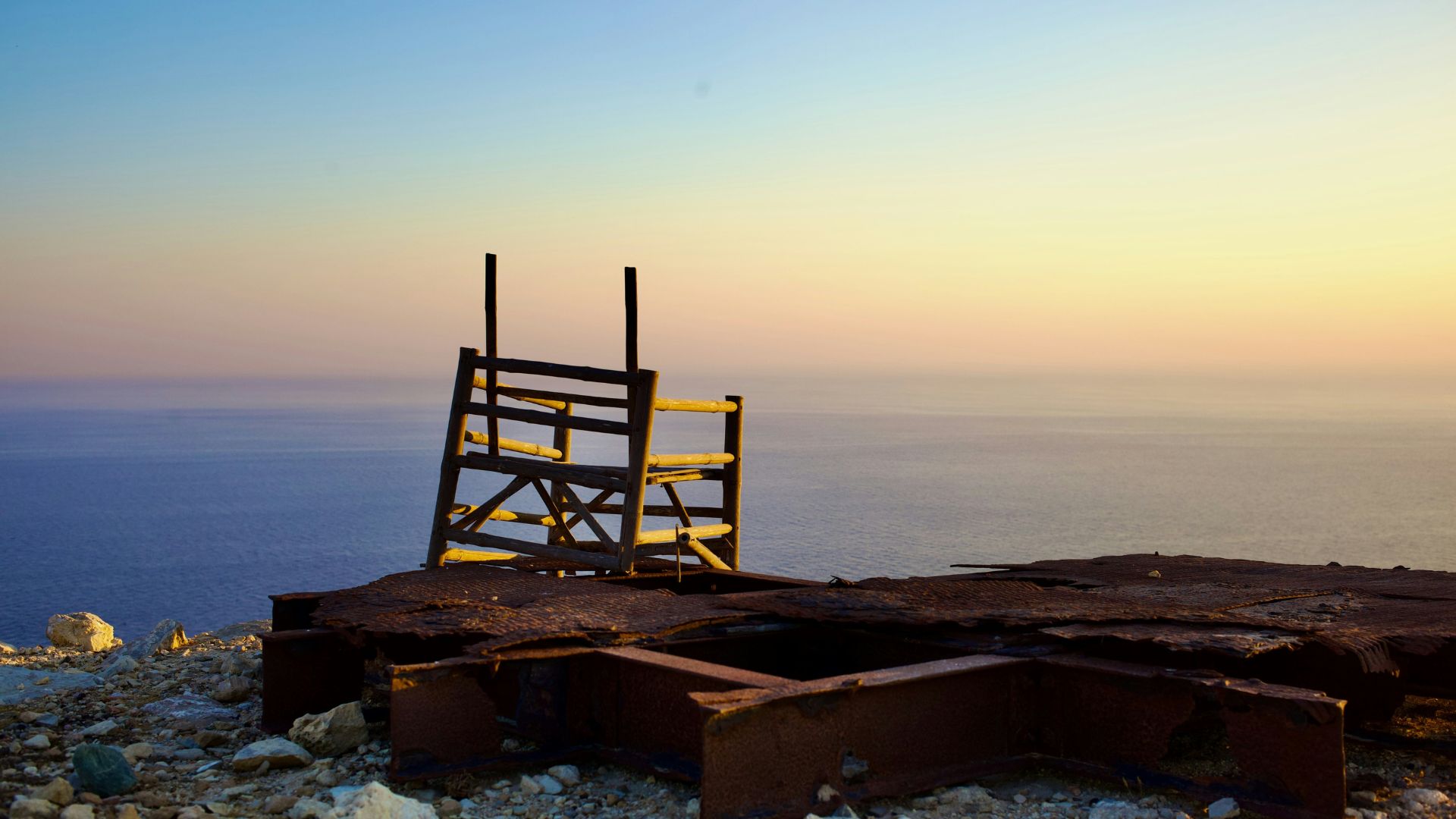 A wooden ladder on a rocky cliff overlooking the sea at sunset.