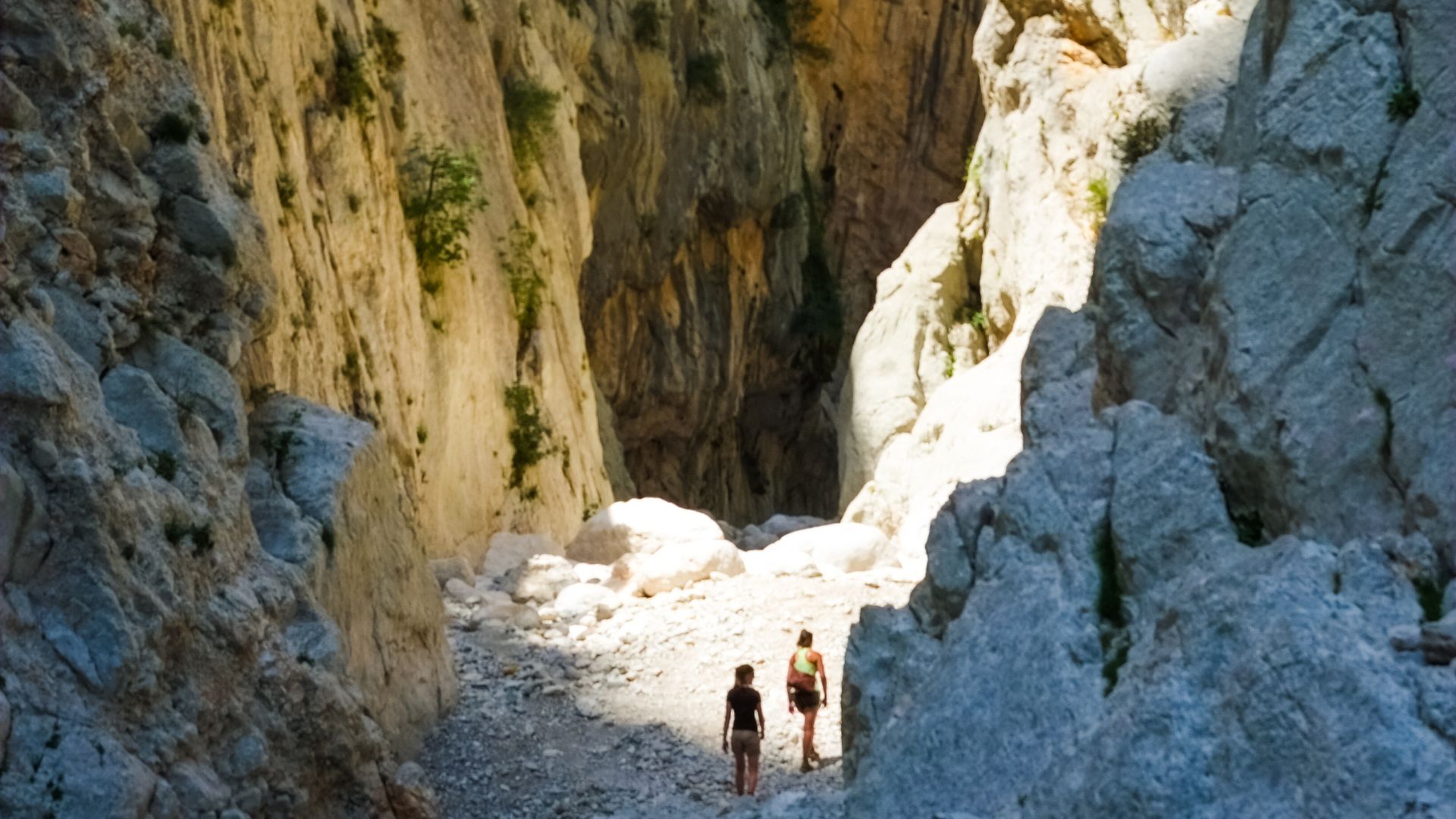 Gola di Su Gorropu, also known as Gorropu Gorge, located in Sardinia, Italy. The image shows two people standing in the gorge, surrounded by tall rock walls