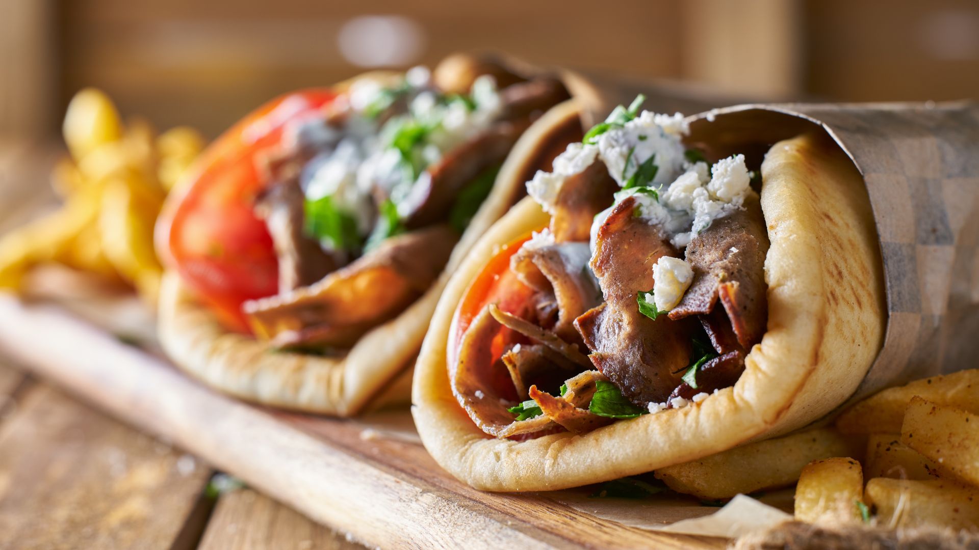 Two gyros sandwiches with fries on a wooden board.