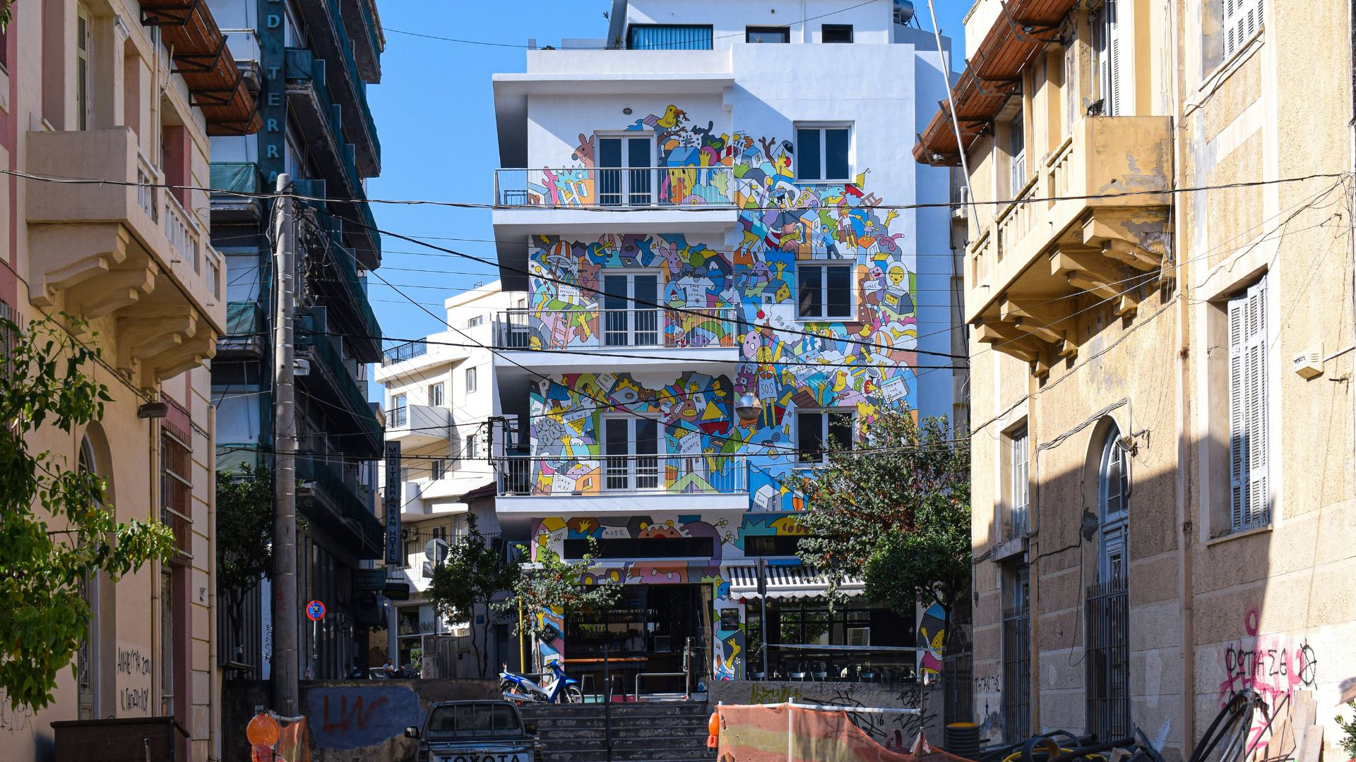 A street view in Heraklion, Crete, featuring buildings with colorful murals.