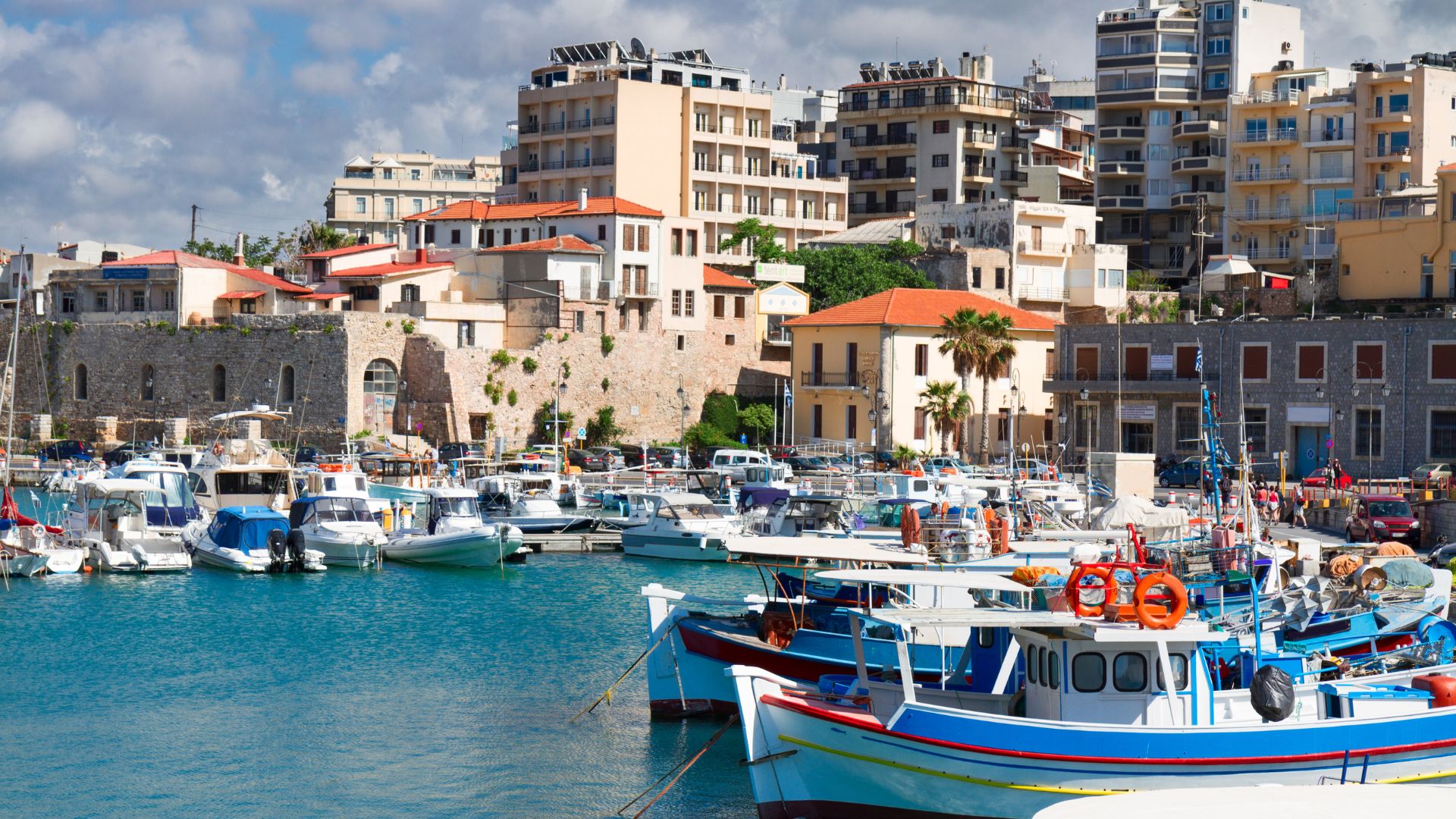 Boats in the harbor of Heraklion, Crete, with buildings in the background.