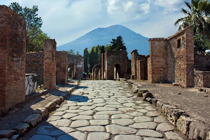 Stone-paved street and ancient ruins at Herculaneum Archaeological Park with Mount Vesuvius in the background.
