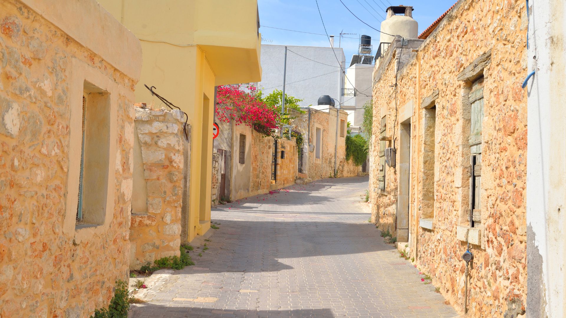 A narrow street in Hersonissos, Crete, with traditional stone buildings on either side.