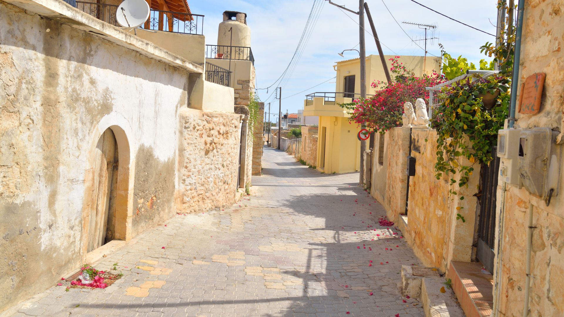 A narrow street in Hersonissos, Crete, with traditional stone buildings on either side.