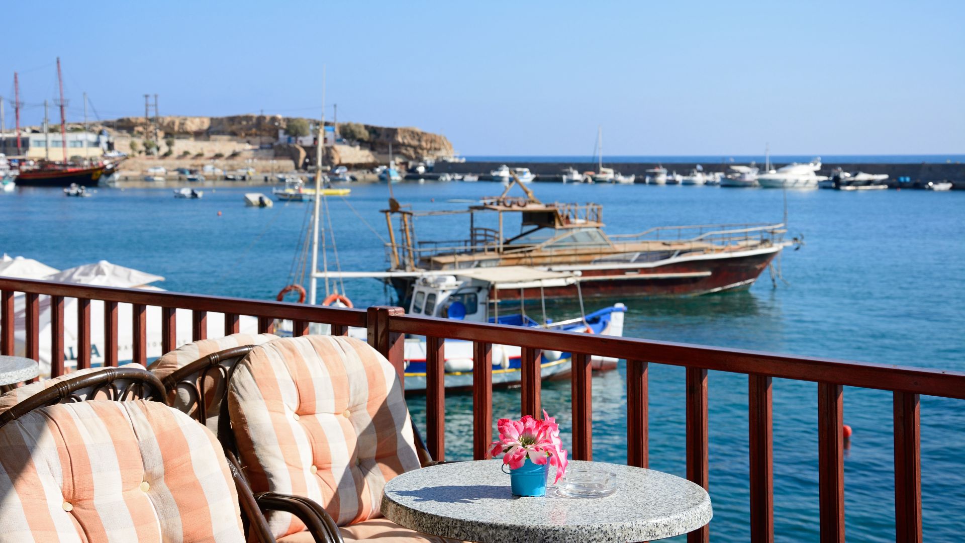 A view from a balcony in Hersonissos, Crete, showing boats in the harbor and the coastline in the background.