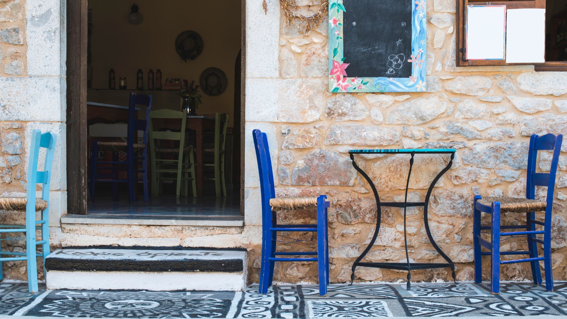 An outdoor seating area with blue wooden chairs and a small table, typical of a kafenio. 