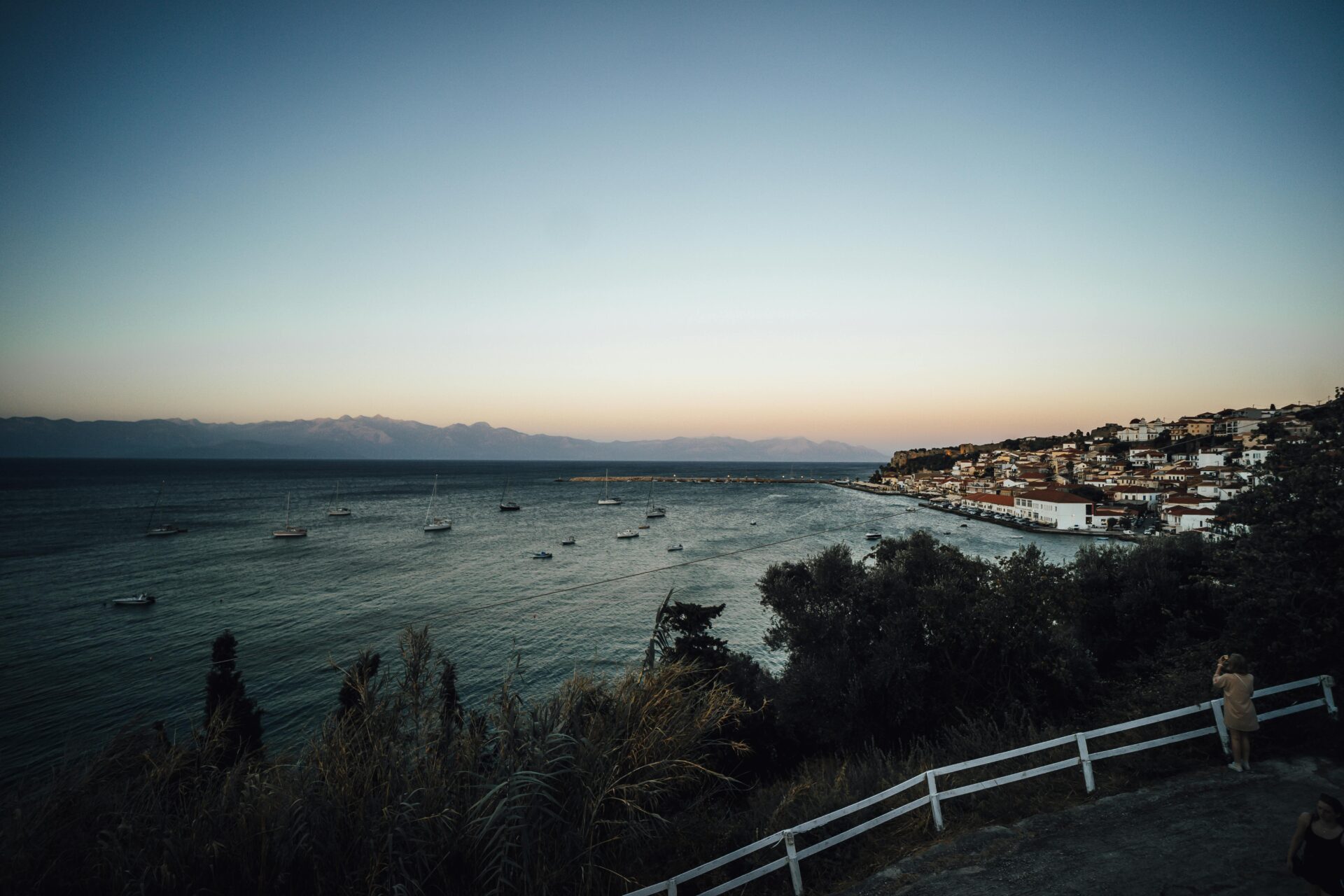 A coastal view of Koroni with traditional houses cascading down a hillside, overlooking the calm blue sea