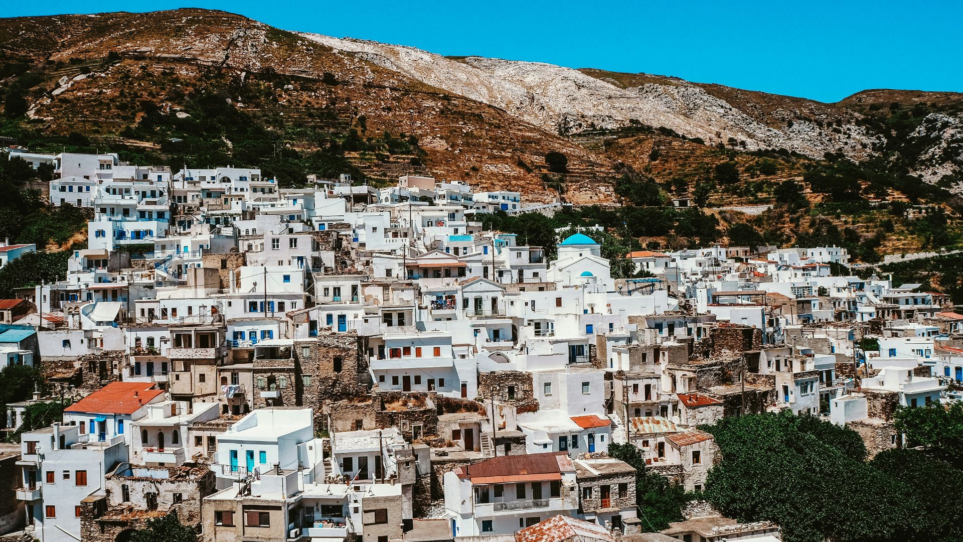 A hillside village with white buildings and a blue-domed church in Naxos, Greece.