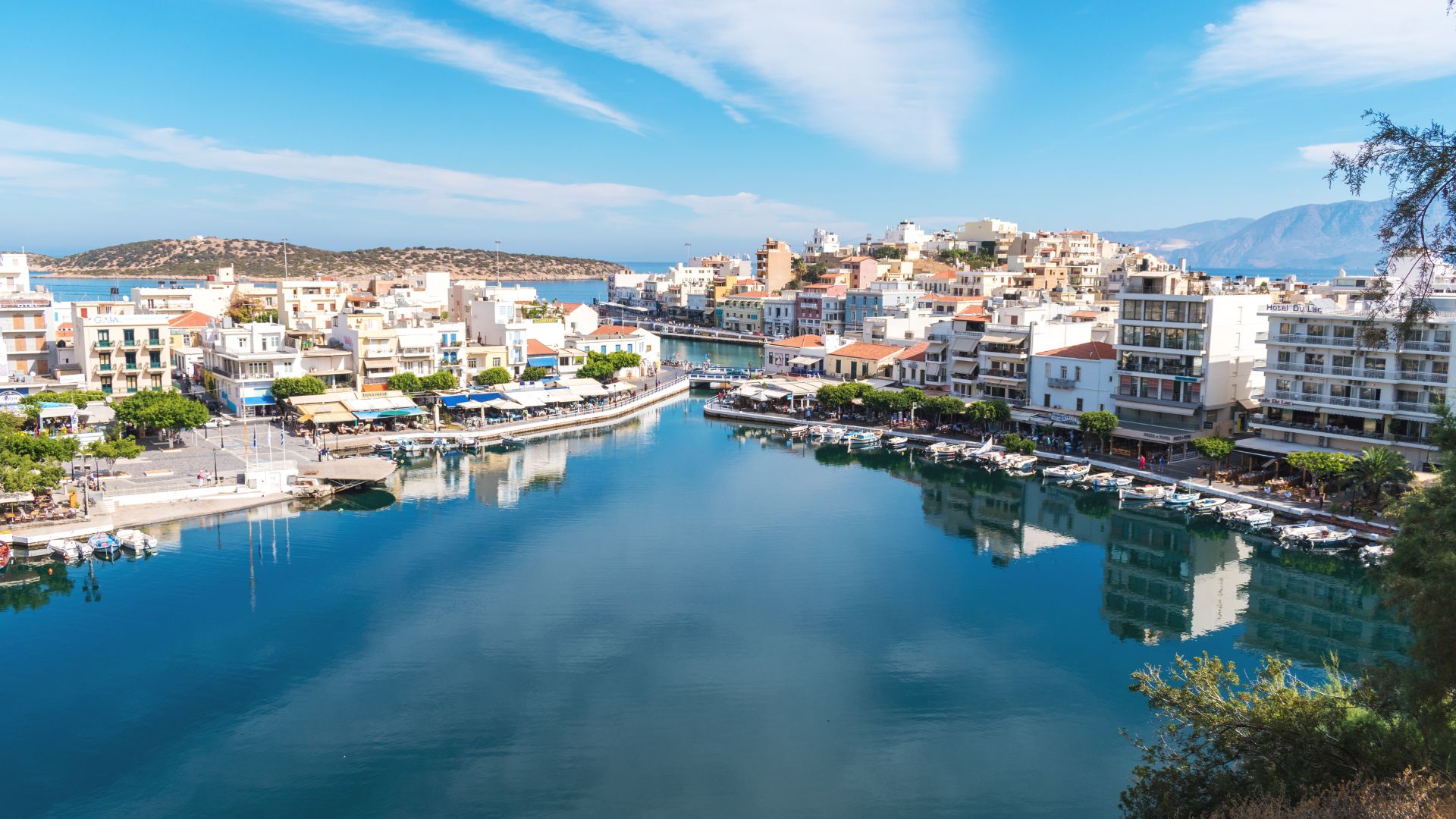 A scenic view of Lake Voulismeni surrounded by buildings and vegetation in Agios Nikolaos, Crete.