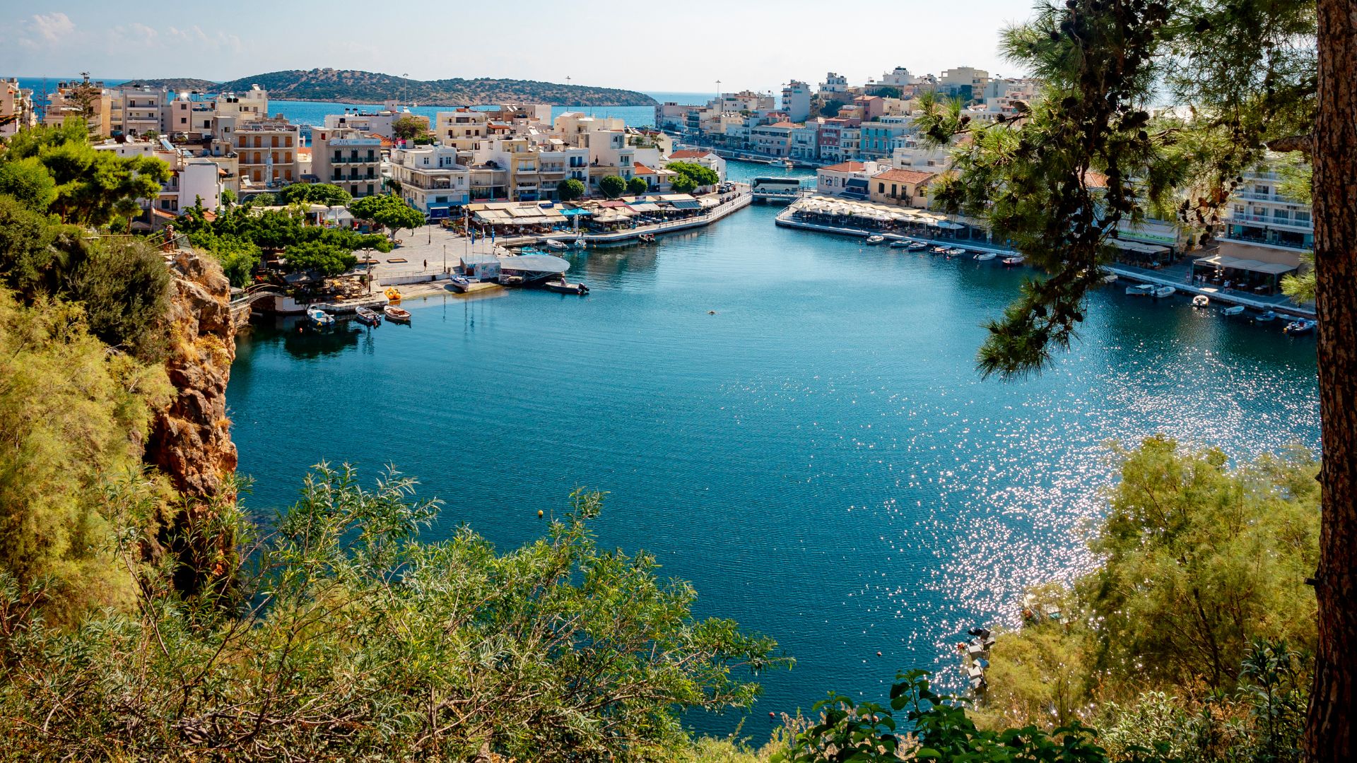 A scenic view of Lake Voulismeni surrounded by buildings and vegetation in Agios Nikolaos, Crete.
