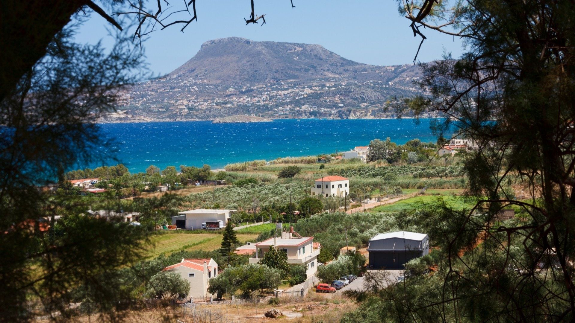 Scenic view of Lefkogia village in Crete, featuring white houses, green landscape, and the sea in the background..