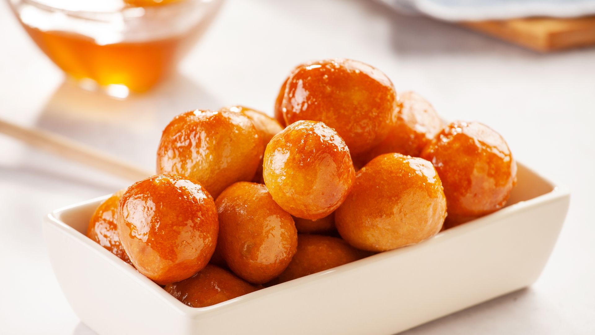 A bowl of golden-brown loukoumades drizzled with honey.