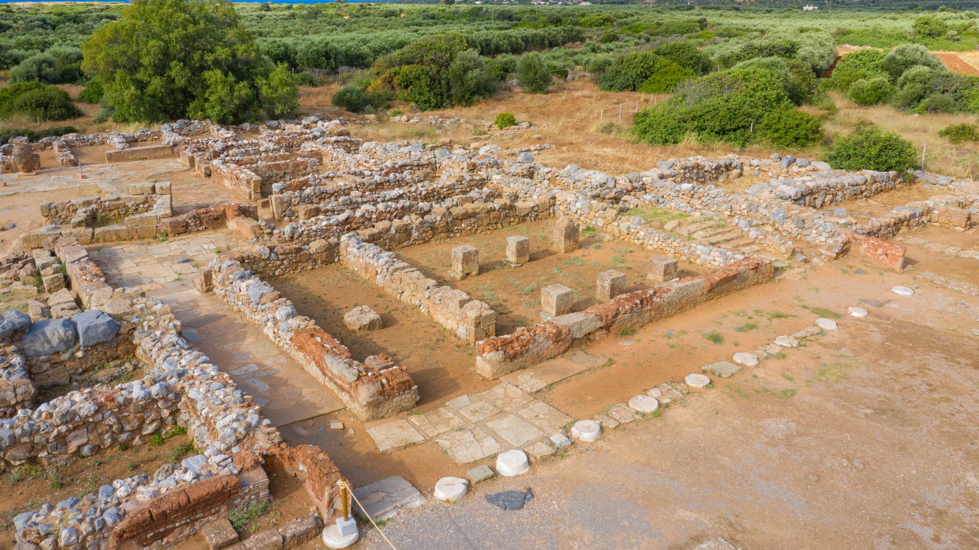 Aerial view of the ruins of the Malia Minoan Palace, an ancient archaeological site in Crete, showcasing the layout of the palace complex with surrounding landscape.