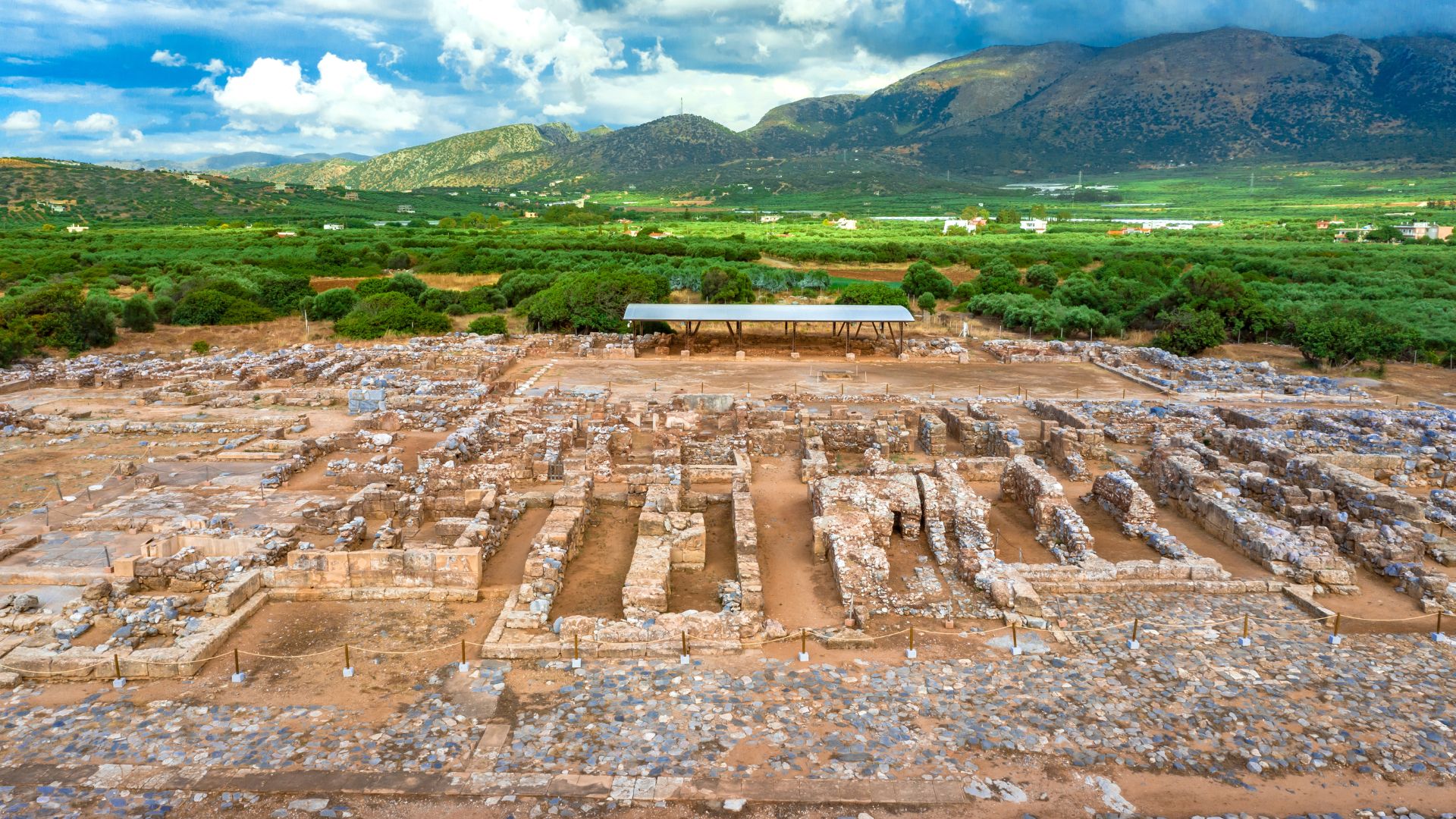 Aerial view of the ruins of the Malia Minoan Palace, an ancient archaeological site in Crete, showcasing the layout of the palace complex with surrounding landscape.