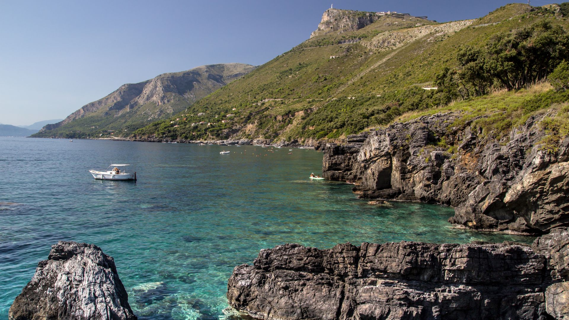 Image shows rocky cliff, blue waters, and editerranean pines cling to the rocks, adding a splash of green against all that blue of  Maratea, Basilicata, Italy.