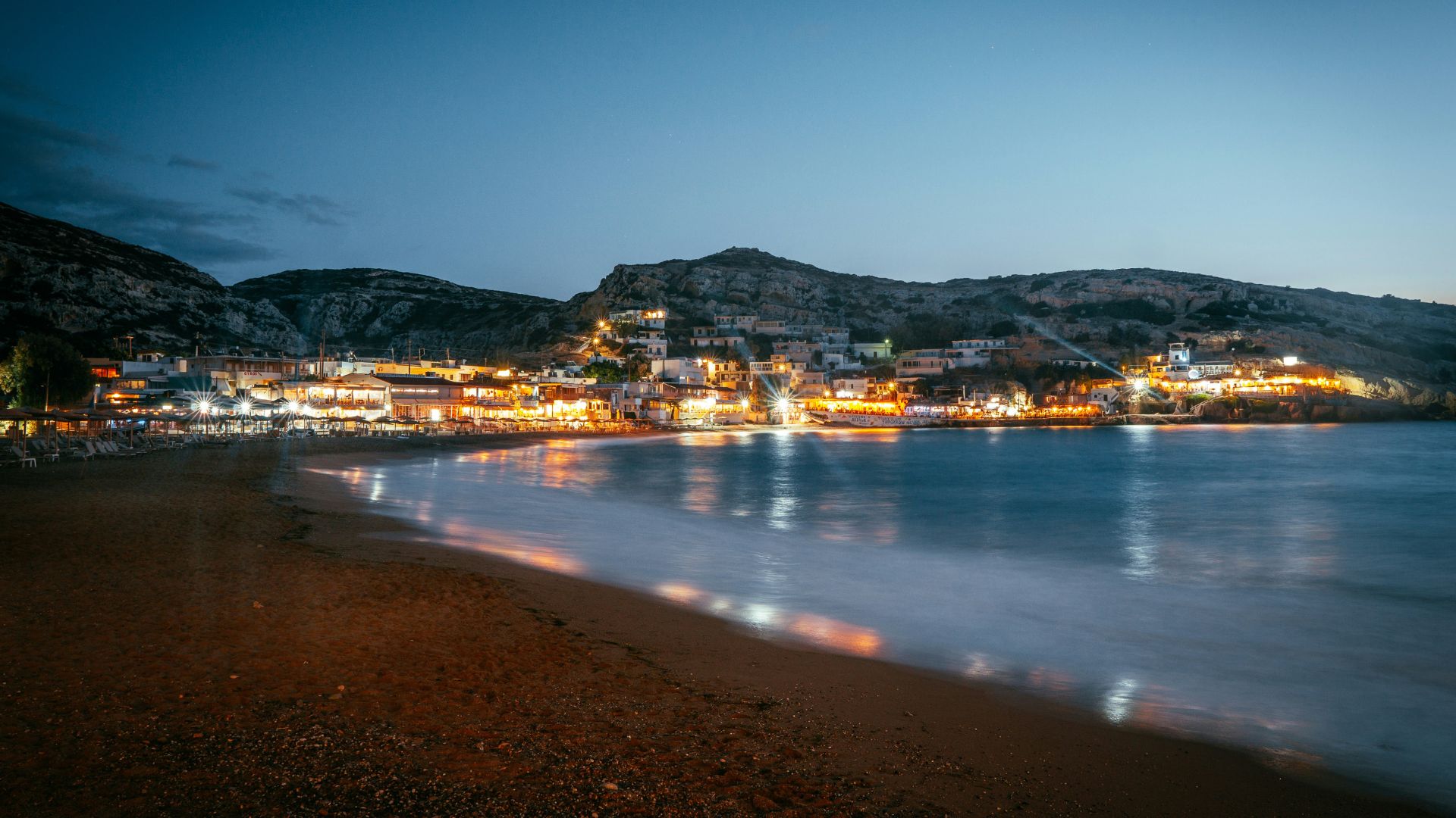 Matala Beach at dusk, with the village lights glowing against the backdrop of the cliffs and the sea.