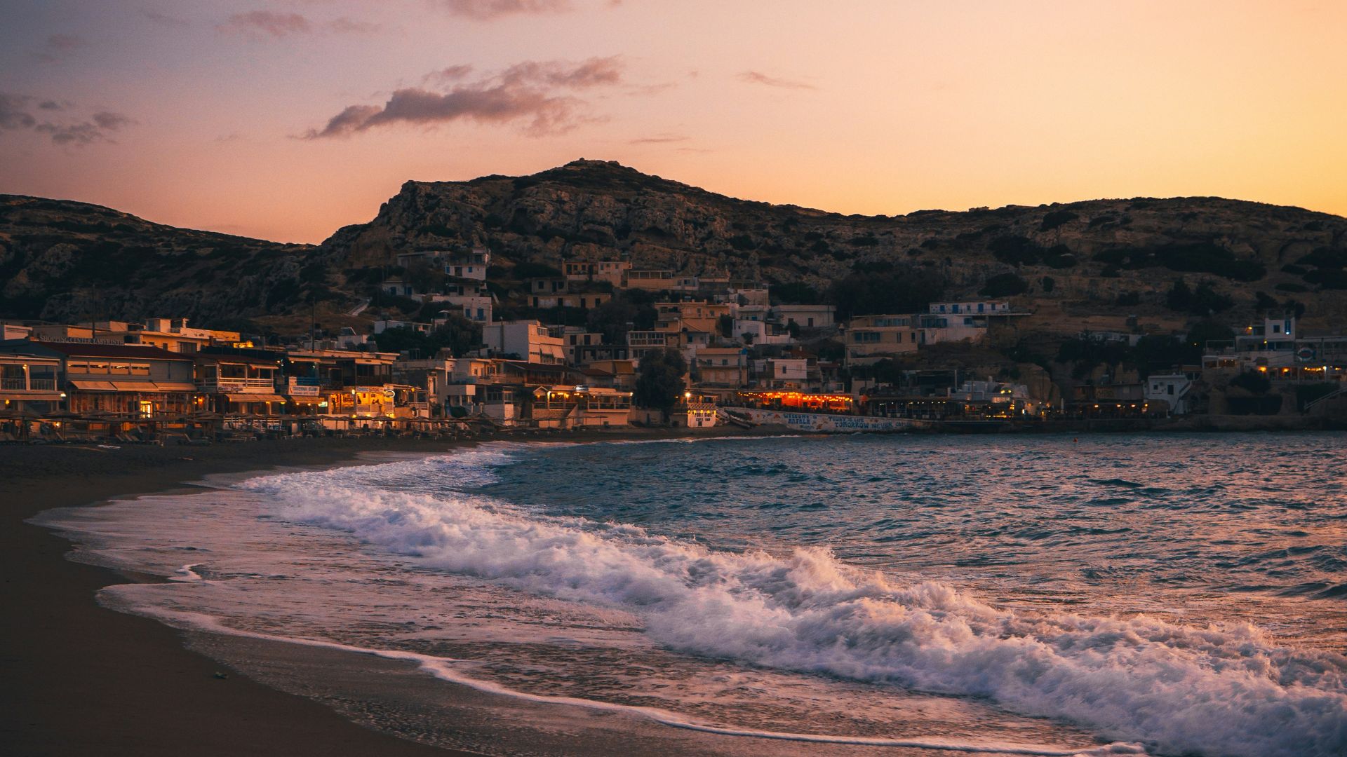 Matala Beach at dusk, with the village lights glowing against the backdrop of the cliffs and the sea.