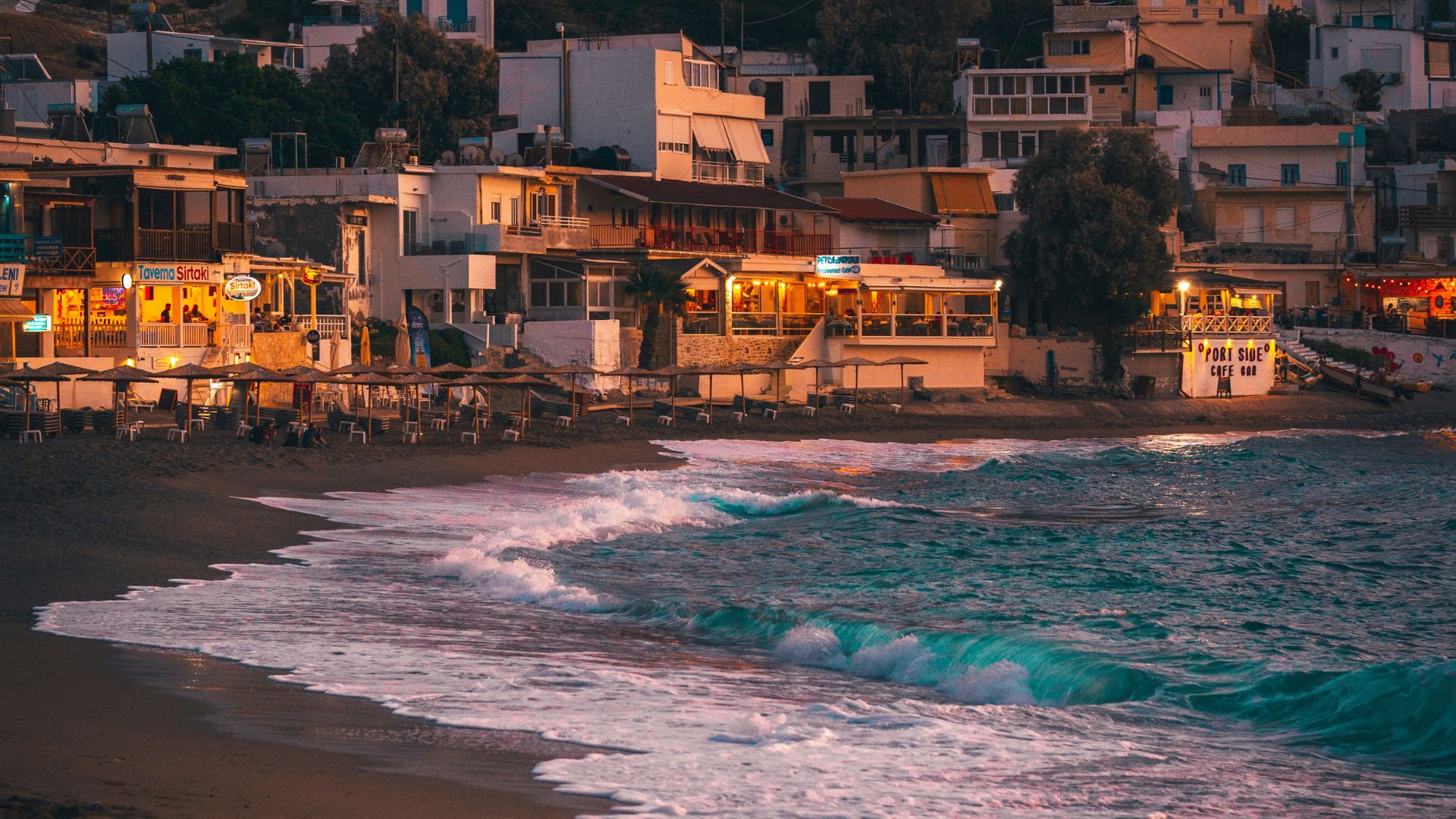 Matala Beach at dusk, with the village lights glowing against the backdrop of the cliffs and the sea.