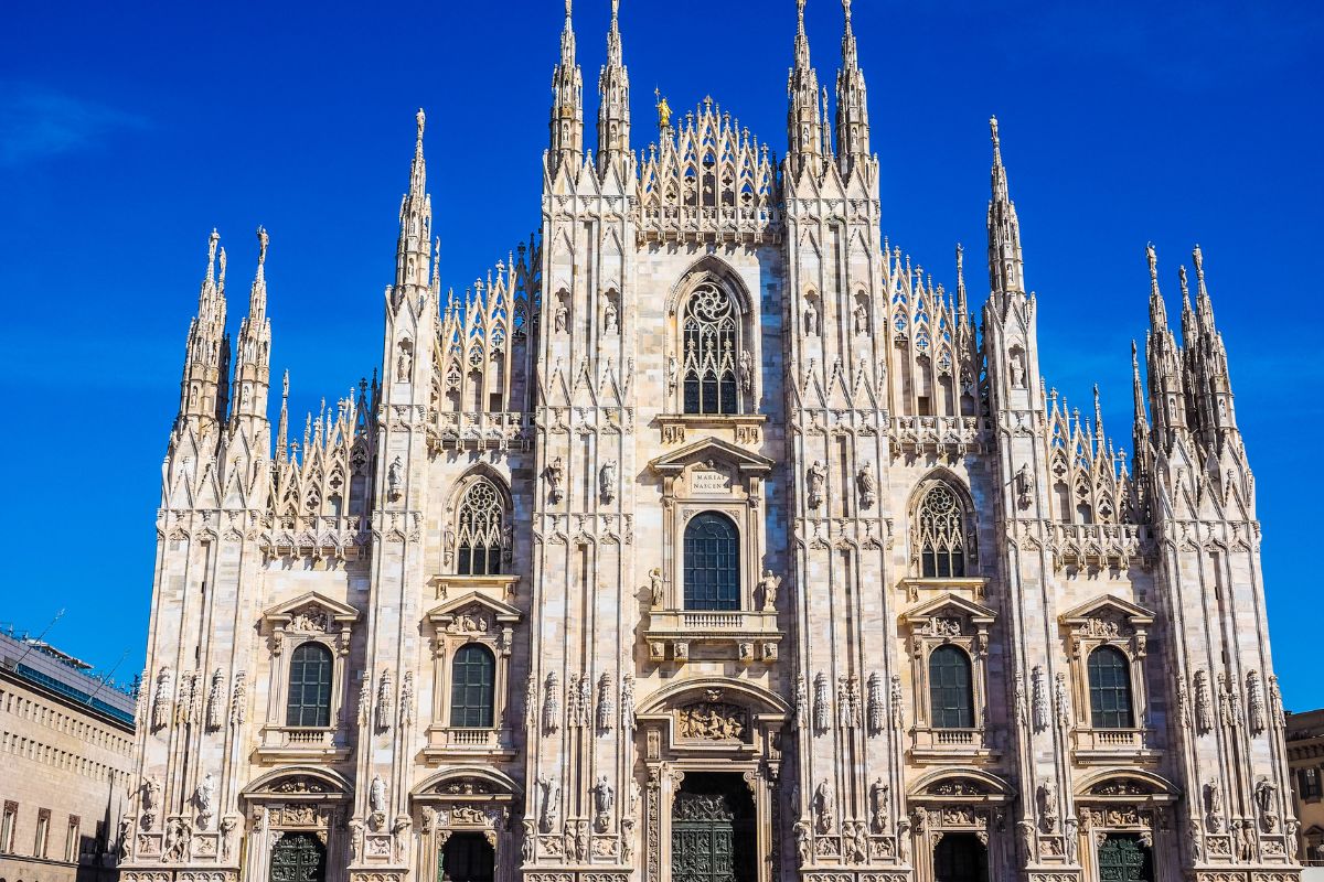 Milan Cathedral, a large Gothic-style cathedral in Milan, Italy. The cathedral is made of white marble and features intricate carvings, spires, and statues.