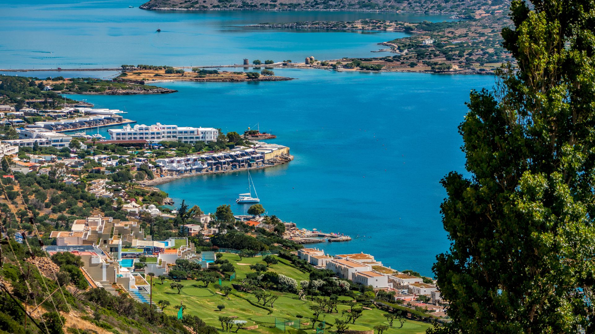 A scenic view of Mirabello Bay with its clear blue waters, coastal towns, and mountainous backdrop in Crete, Greece.
