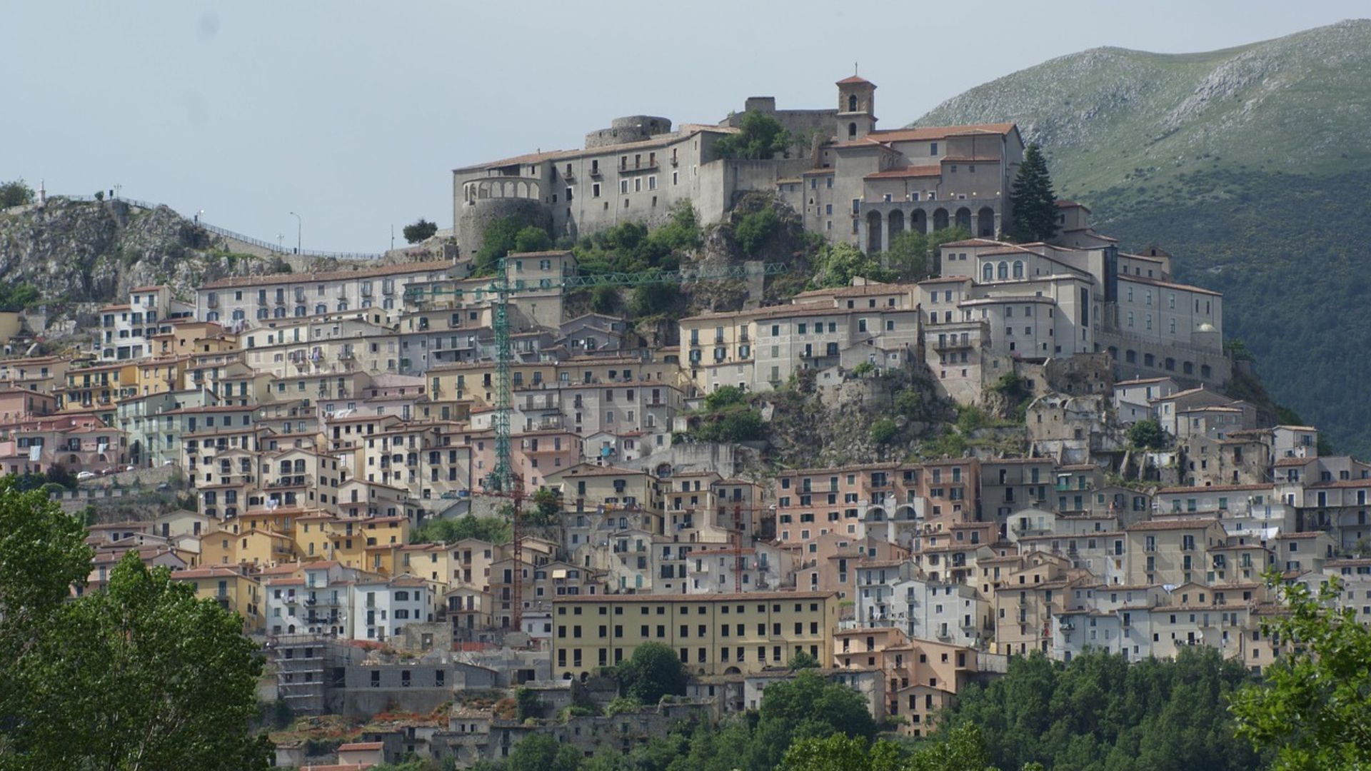 The image shows Muro Lucano, a town in the Basilicata region of Southern Italy characterized by its hilltop location and densely packed buildings. .