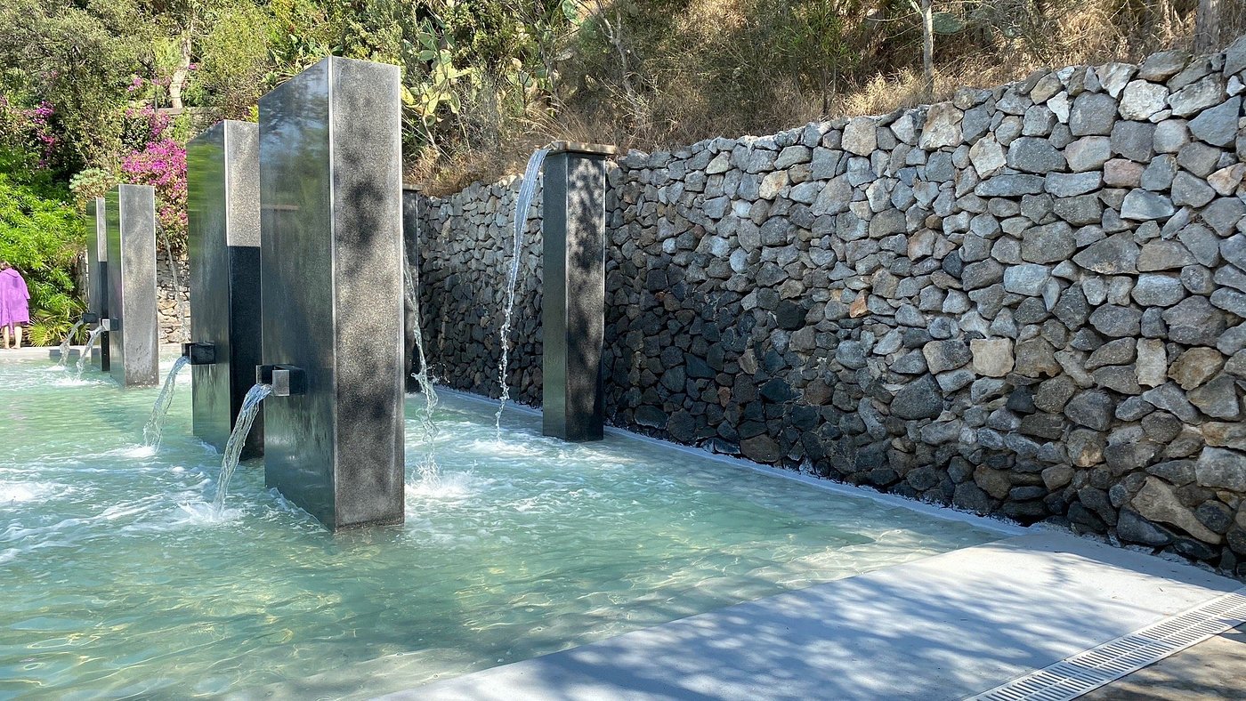 Water features and stone walls at Negombo Thermal Park in Italy, surrounded by lush greenery.