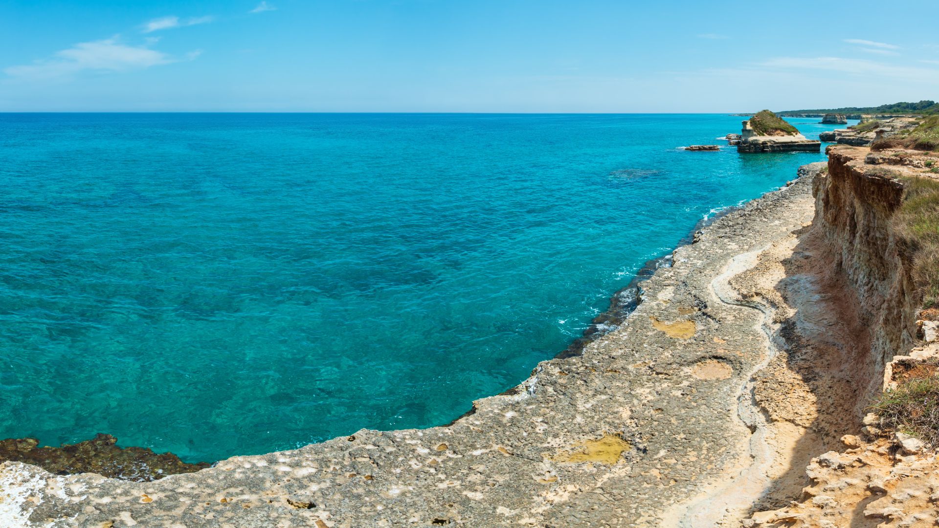 The rocky coastline of Capo Caccia meets the turquoise waters of the Adriatic Sea near Neptune's Grotto in Sardinia, Italy.