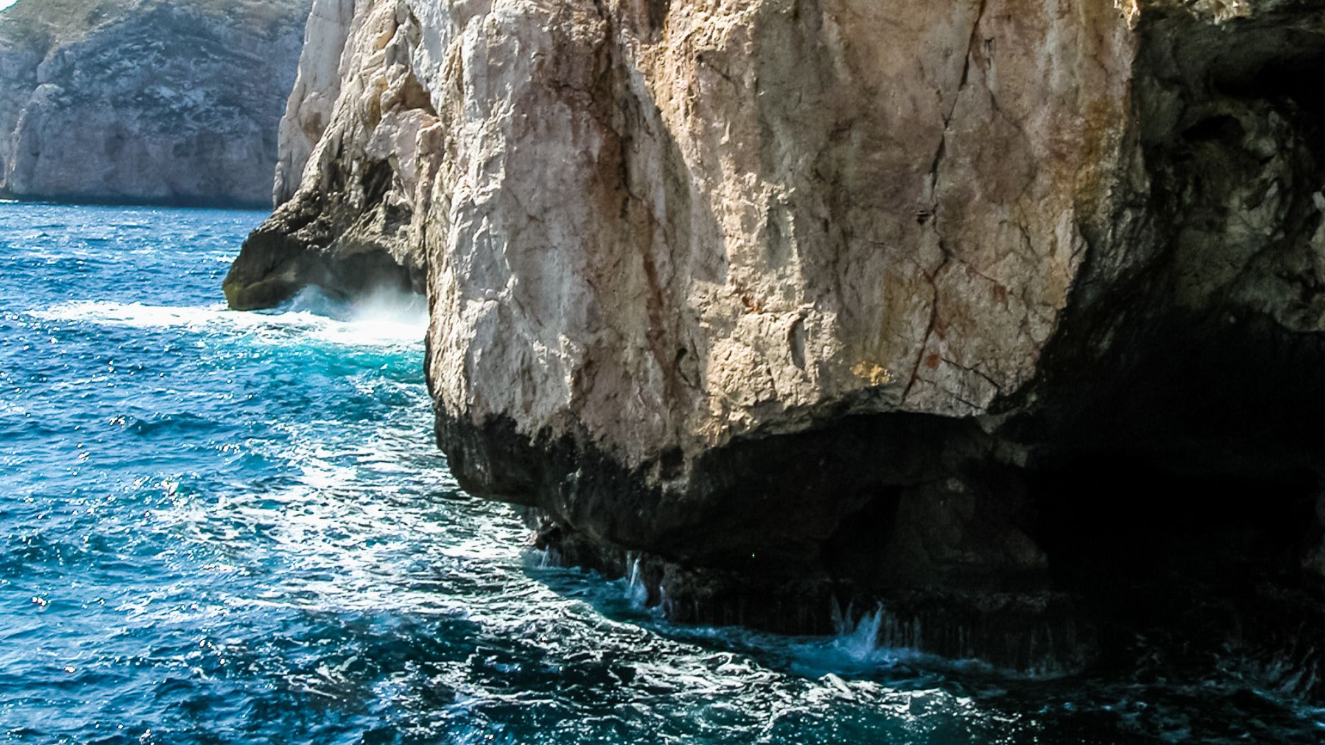 A rocky cliff face meets the blue waters of the Mediterranean Sea at Neptune's Grotto in Sardinia, Italy.