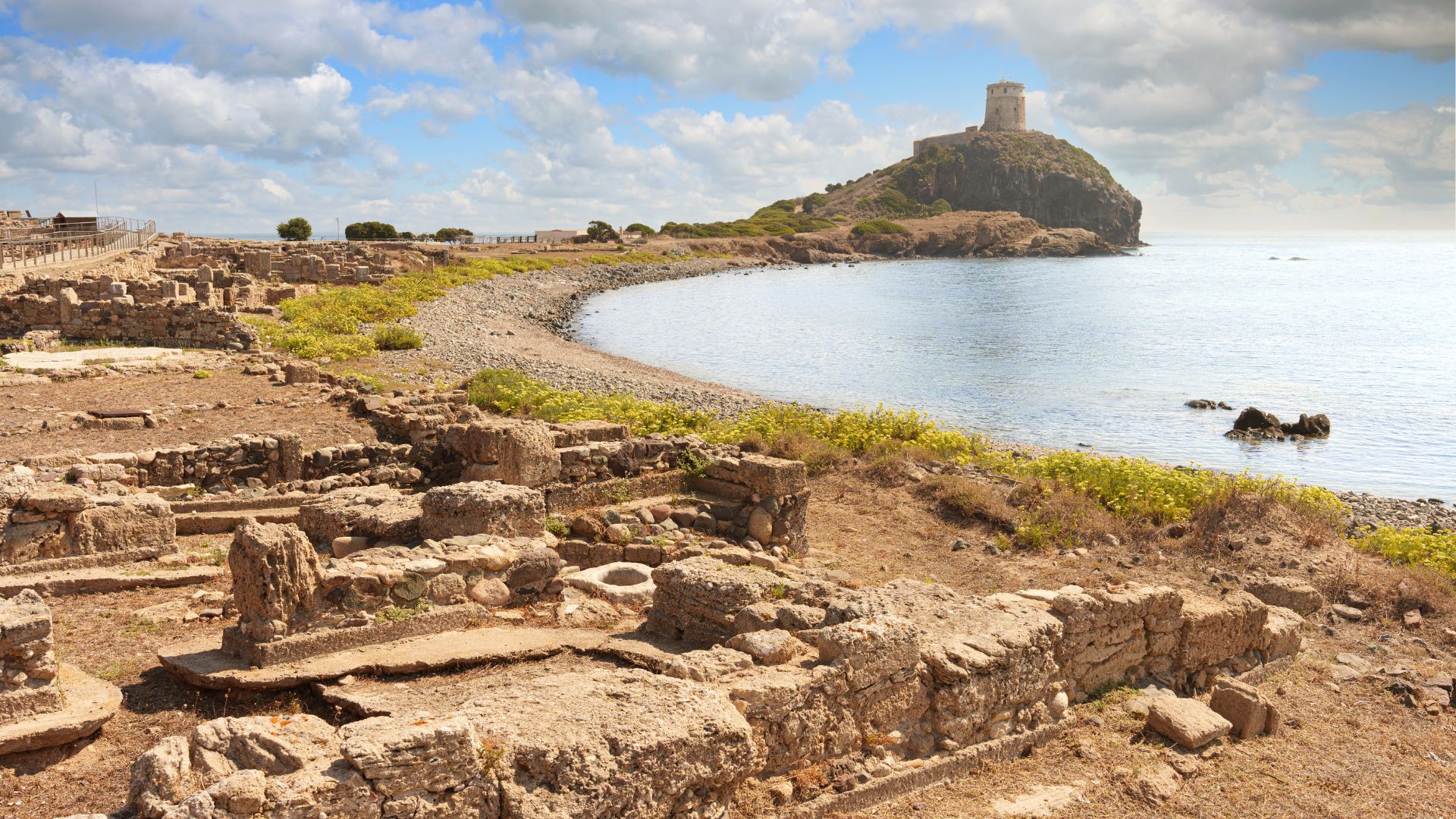 Scenic view of a tower perched on a cliff, greenery, still water, and ruins in Nora in Cagliari, Sardinia, Italy. 