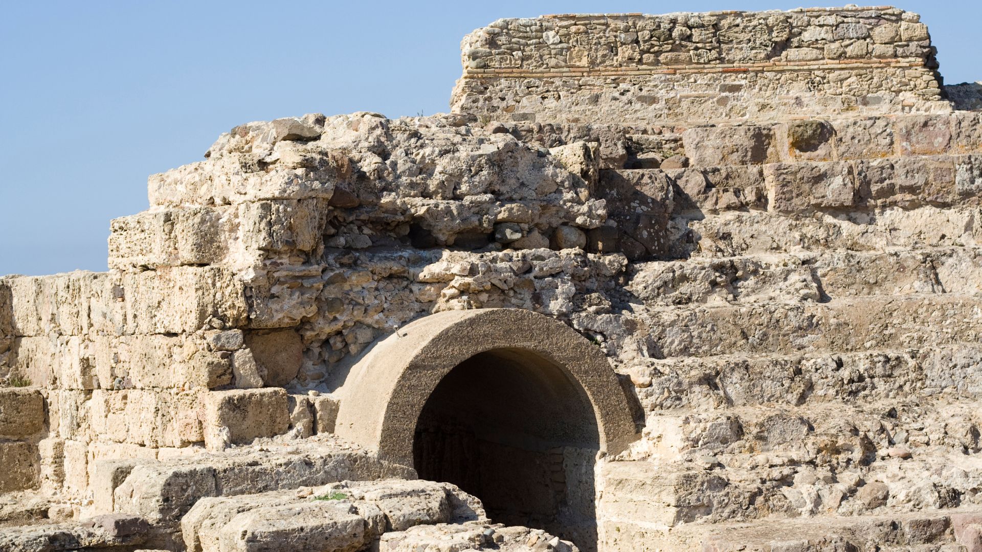  Ancient stone ruins with an arched entrance at the archaeological site of Nora, Sardinia, under a clear blue sky