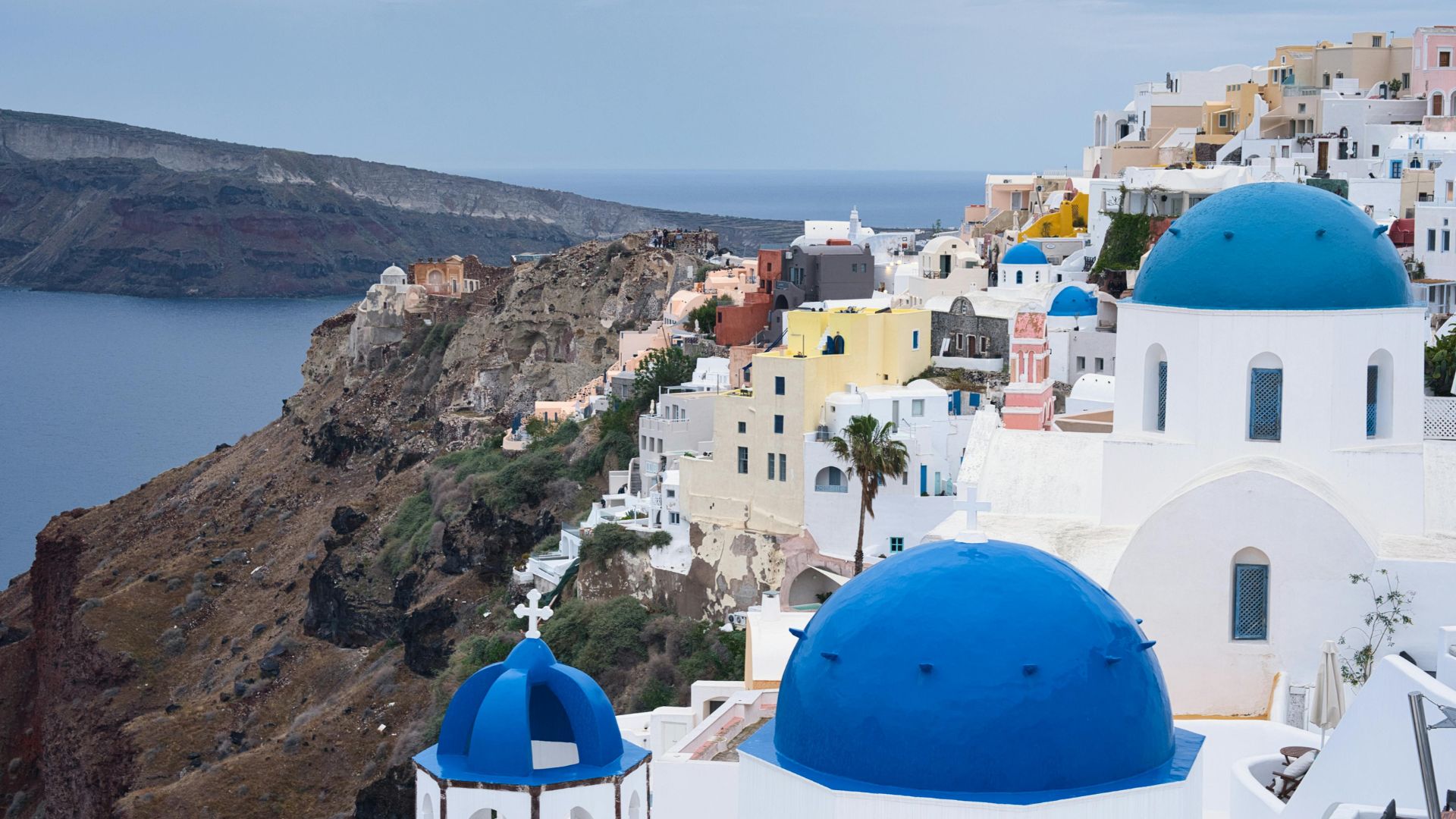 Santorini caldera with white buildings and blue domes on cliffs overlooking the sea.