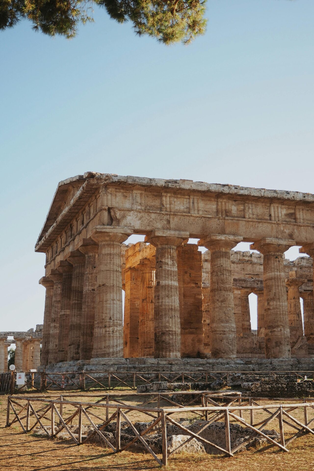 Ancient Greek temple ruins in Paestum, Italy, with tall stone columns under a clear blue sky.