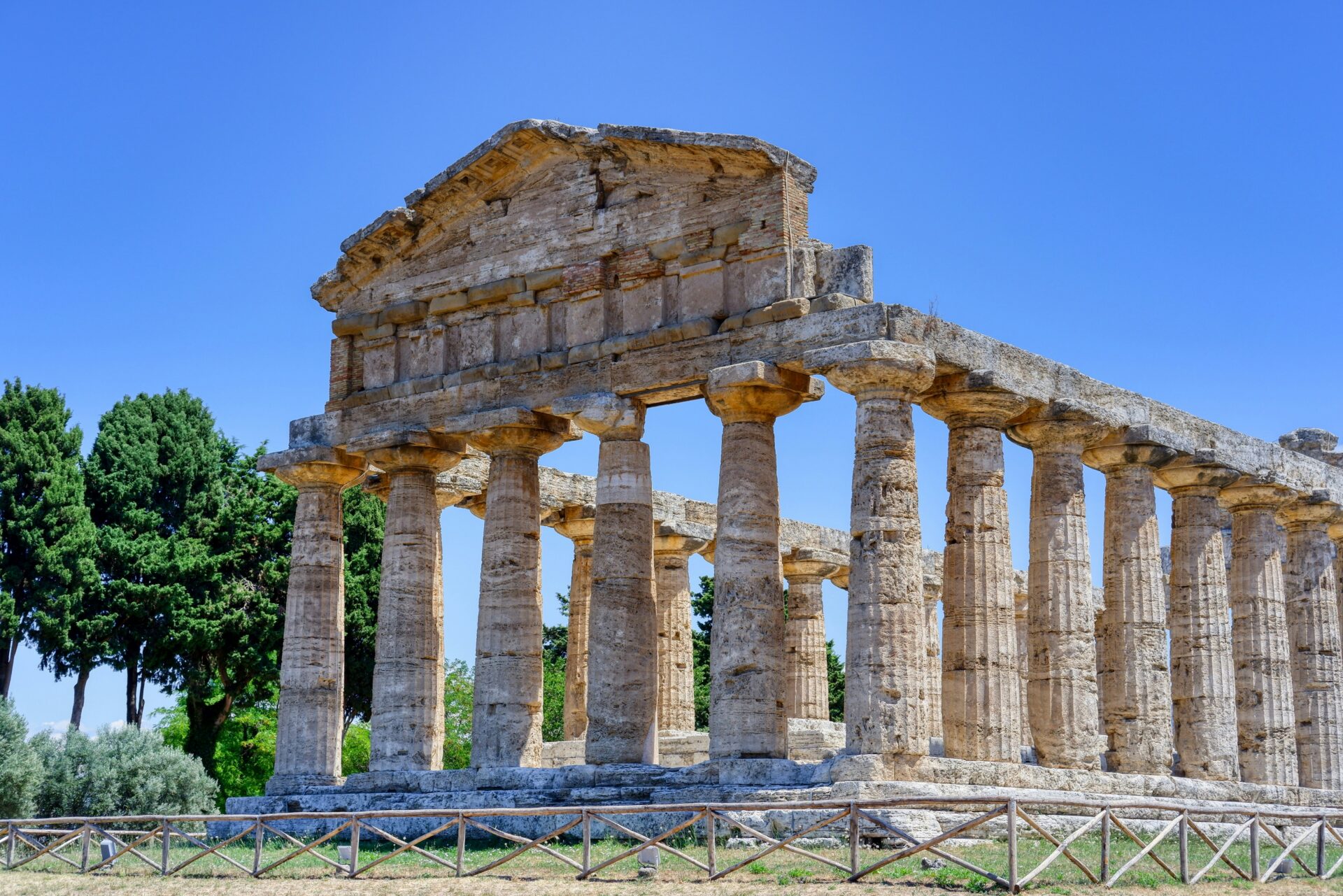 Ancient Greek temple ruins in Paestum, Italy, with tall stone columns and a clear blue sky.