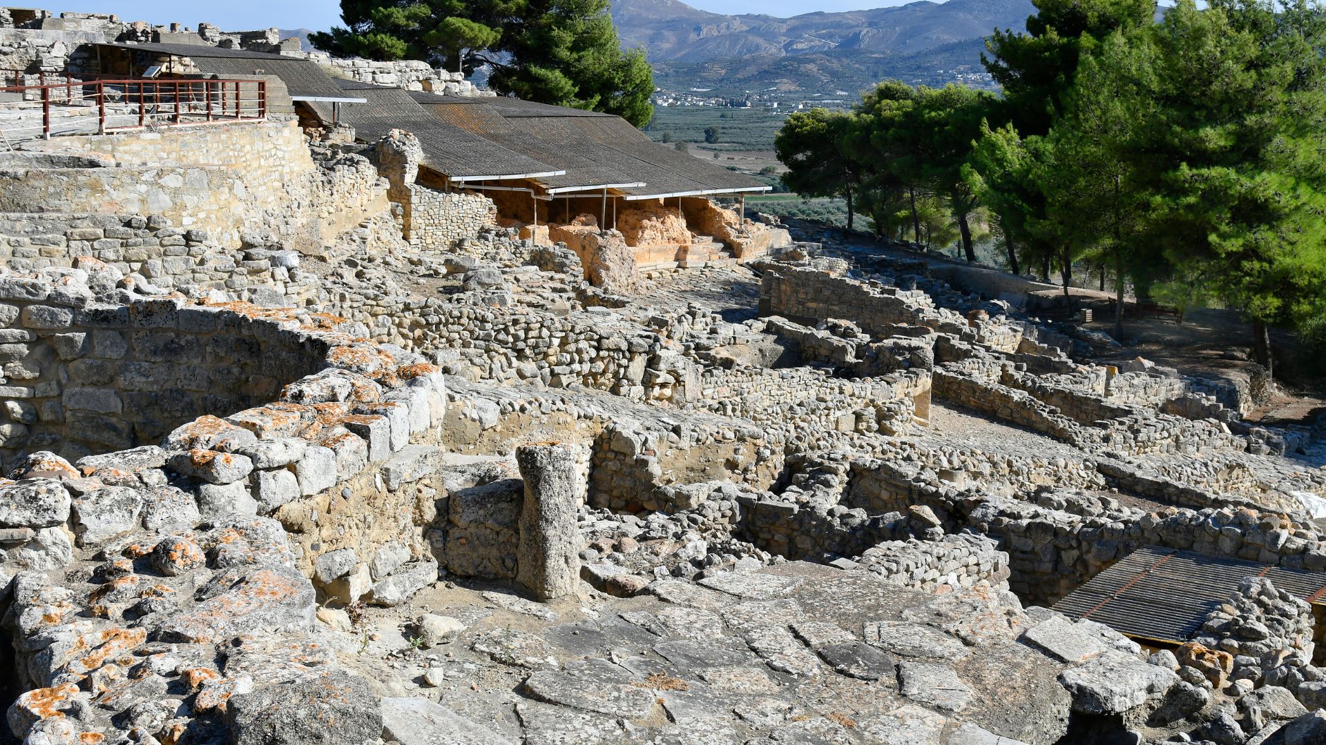 Ruins of the ancient Minoan palace of Phaistos on a hillside in Crete, featuring stone walls and remnants of structures.