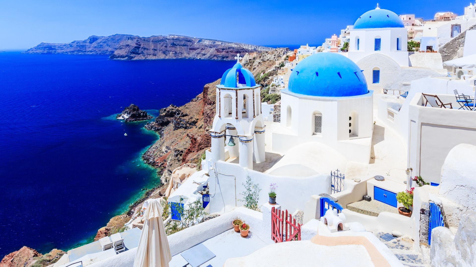 Whitewashed buildings with blue domes in Santorini, Greece, overlooking the Aegean Sea.
