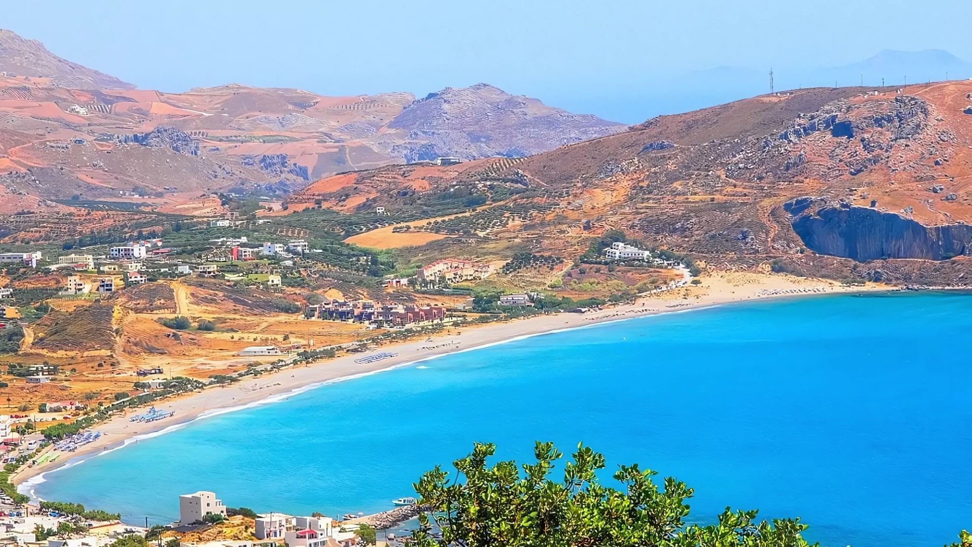 Plakias beach in Crete features a long sandy shoreline bordered by the turquoise waters of the sea and rugged hills.