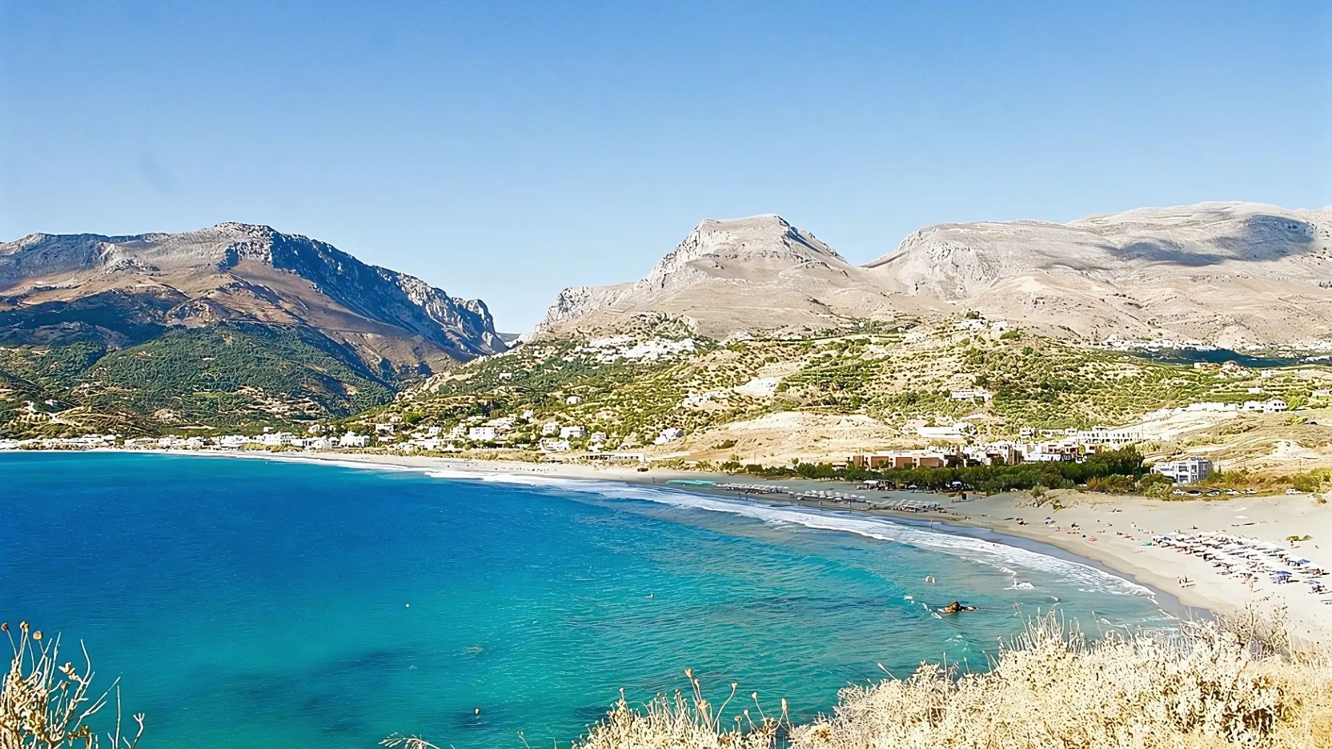 Plakias beach in Crete features a long sandy shoreline bordered by the turquoise waters of the sea and rugged hills.
