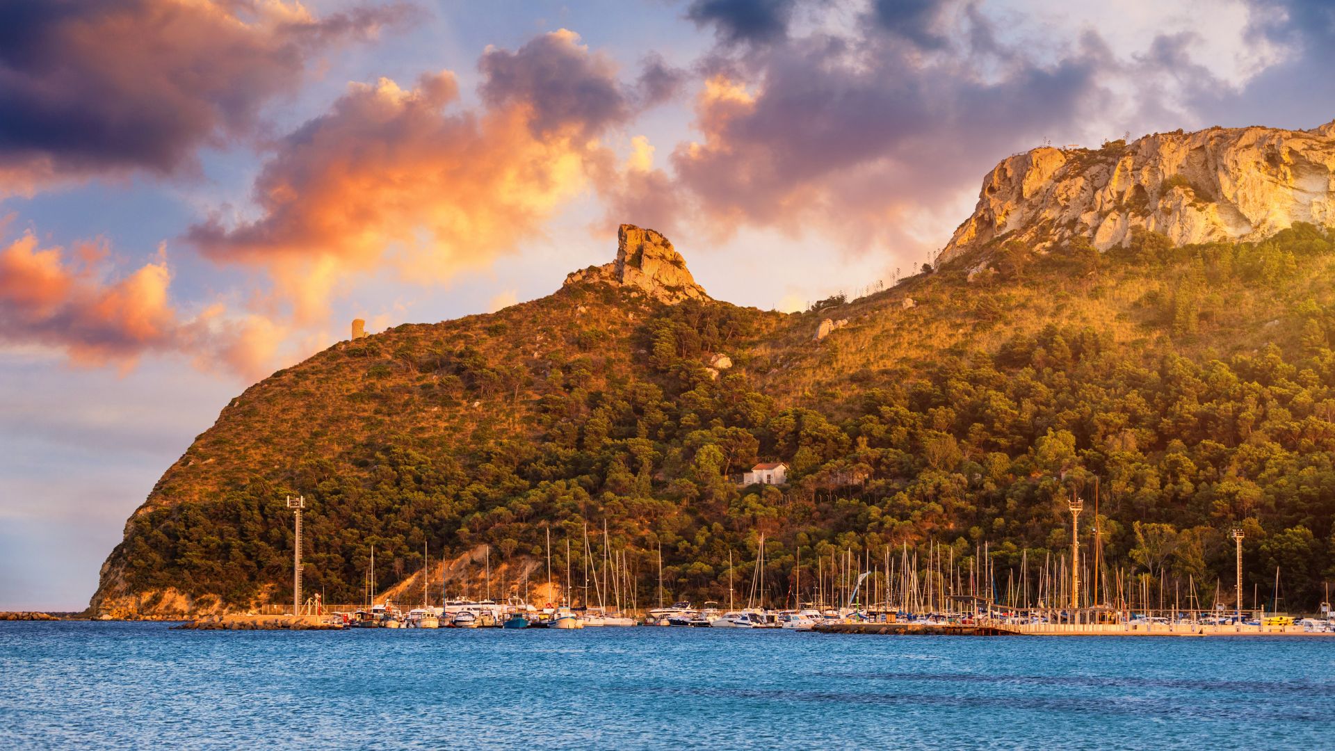Scenic view of Poetto Beach in Cagliari, Sardinia, Italy, with the Sella del Diavolo promontory overlooking the coastline and numerous boats anchored in the sea.
