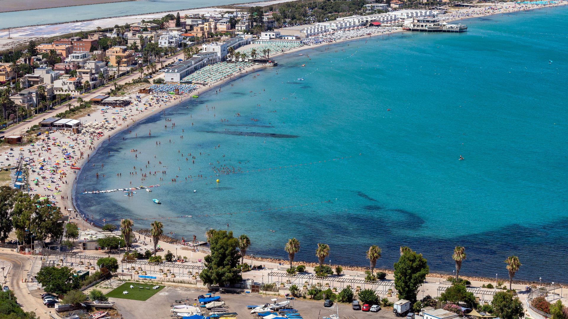 Aerial view of Poetto Beach in Cagliari, Sardinia, showcasing the coastline, beachgoers, and surrounding urban area.