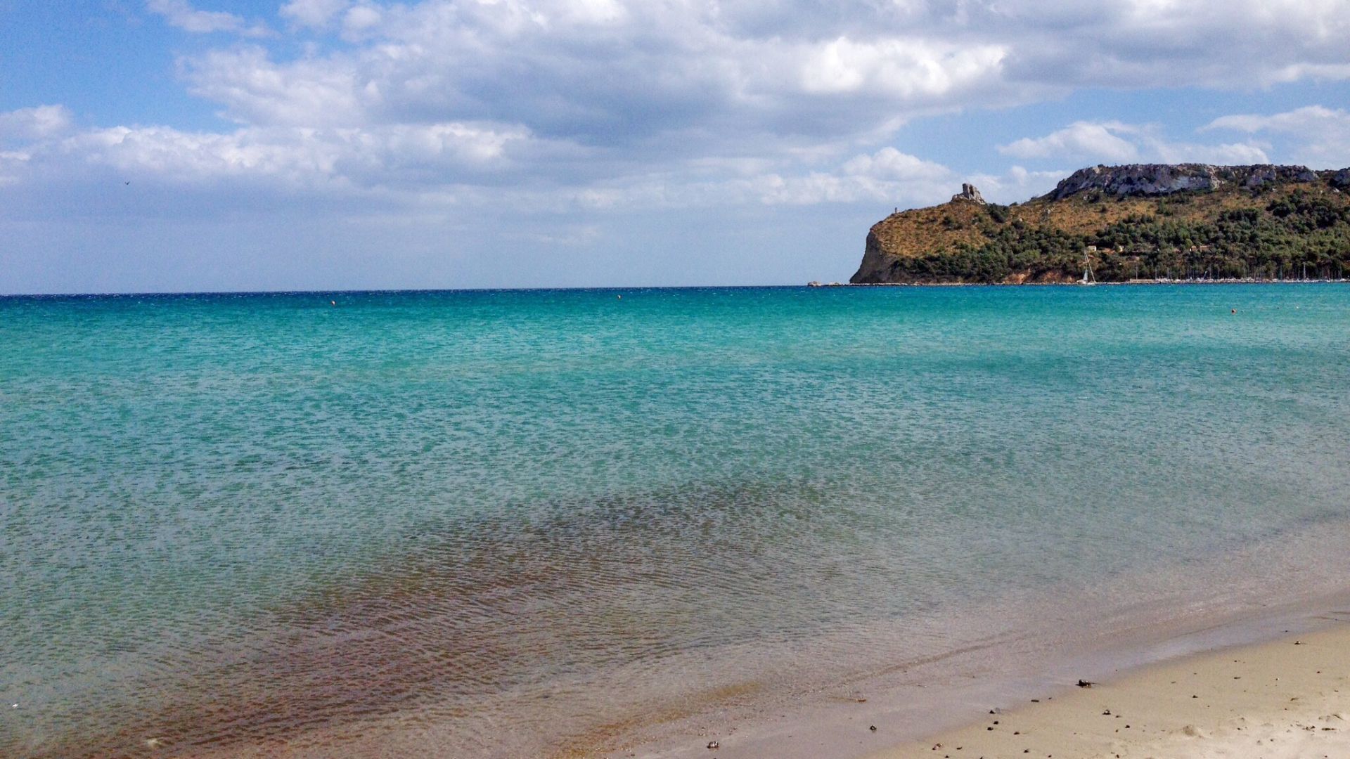 Scenic view of Poetto Beach in Cagliari, Sardinia, featuring the Sella del Diavolo promontory, clear turquoise water, and a sandy beach.