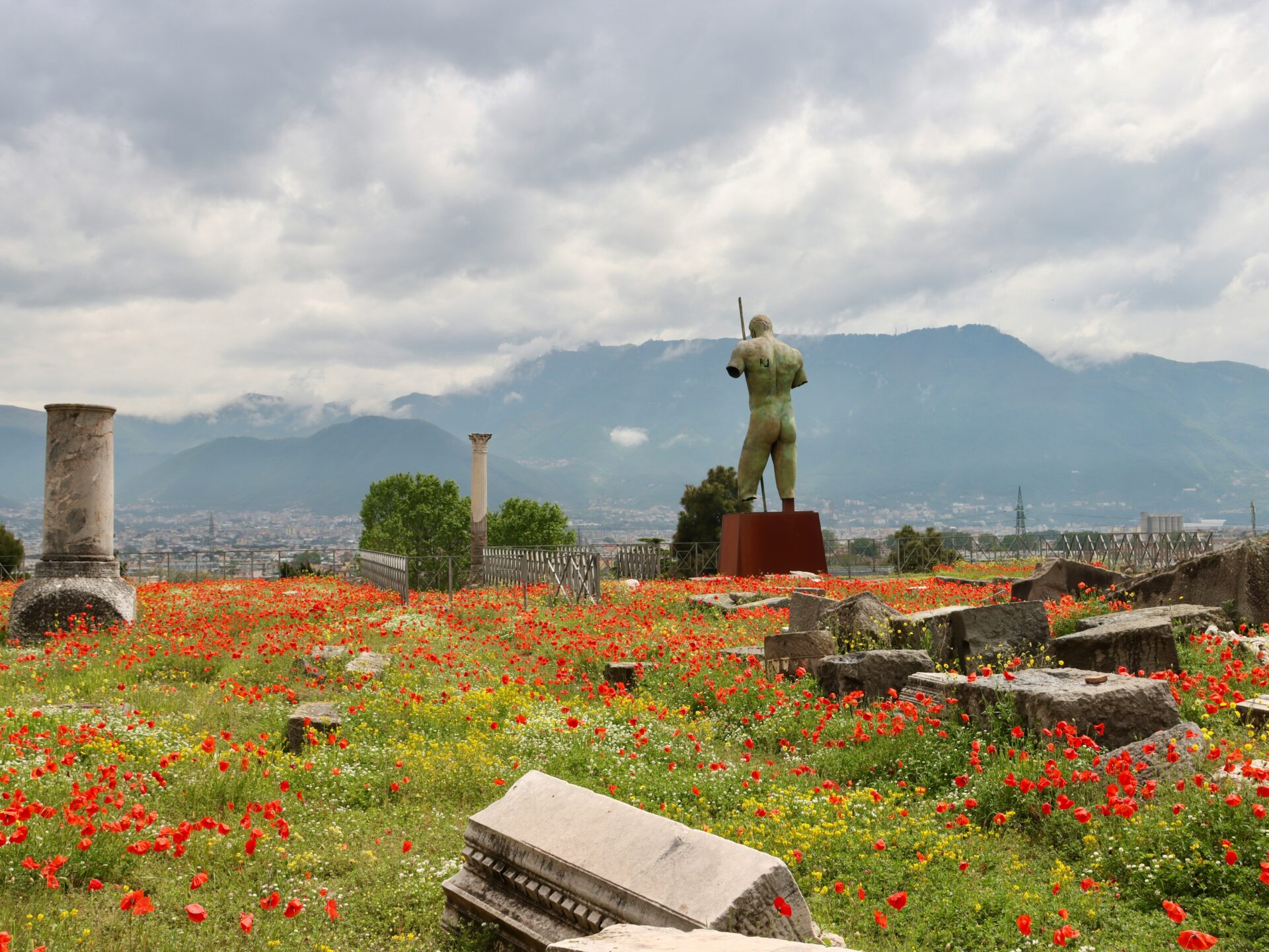 Colorful flower-filled garden with ancient ruins and a statue at the archaeological site of Pompeii, Italy.