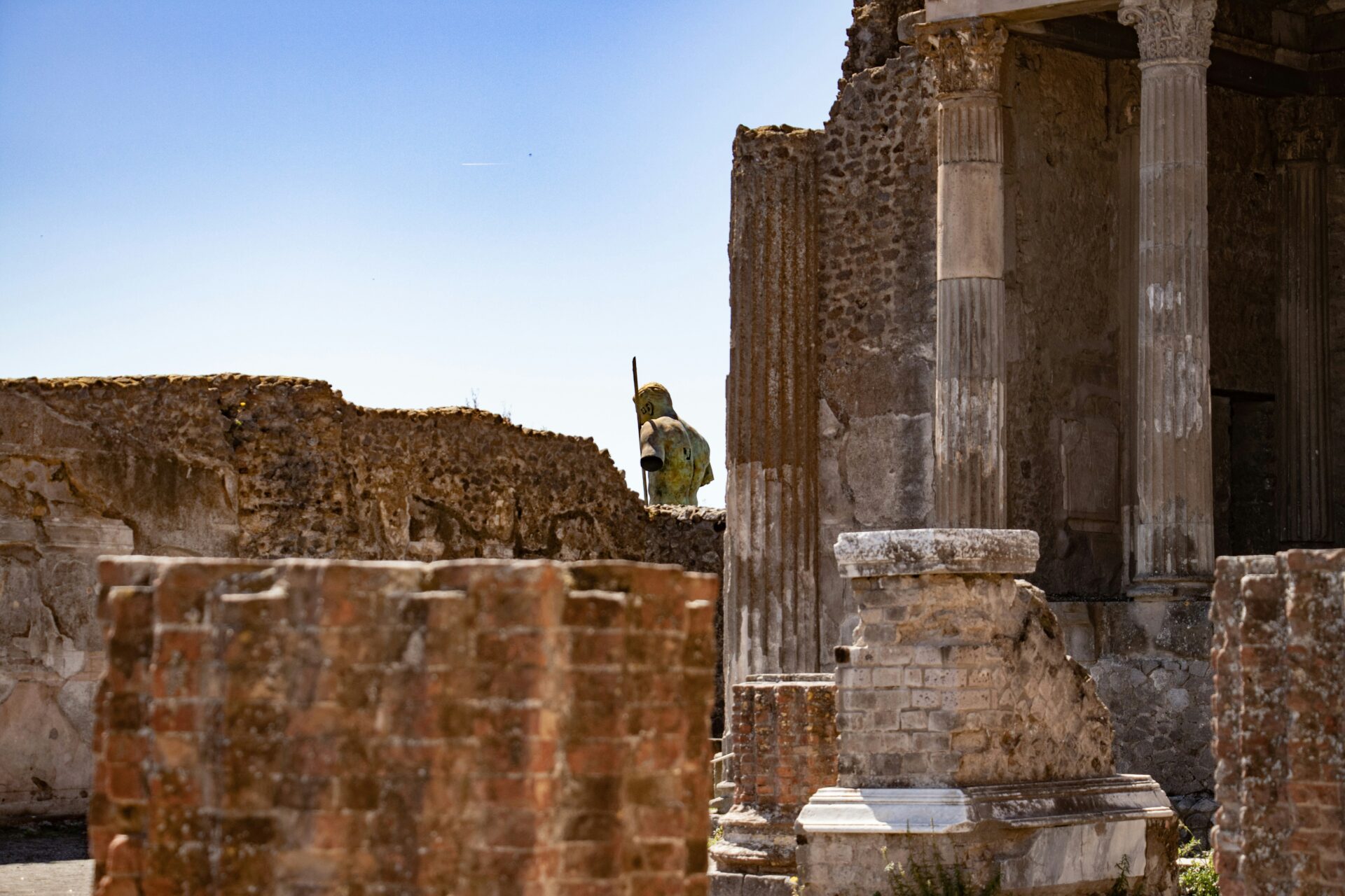 Ancient ruins and statue in Pompeii, Italy, under a clear blue sky.