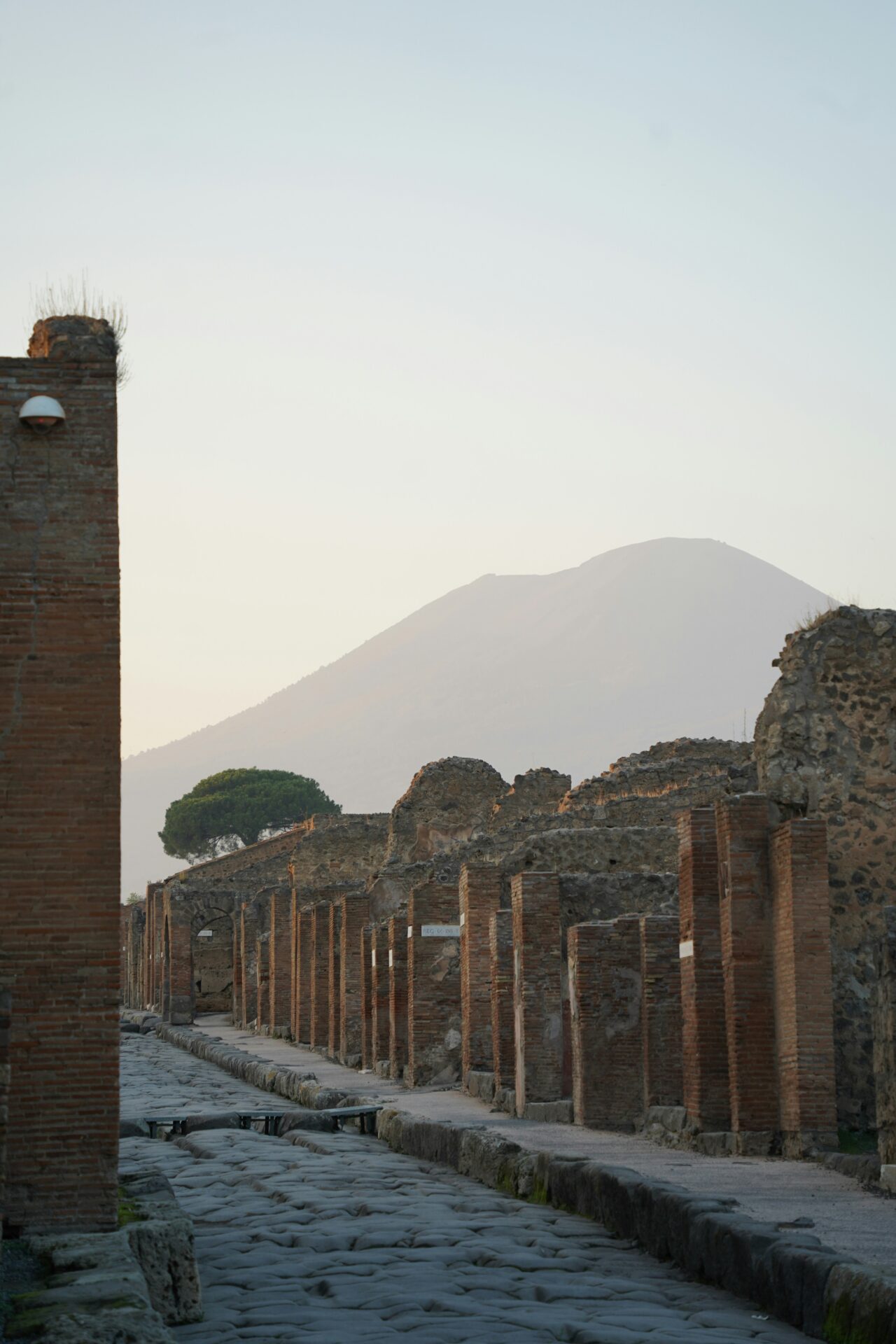 Ancient stone street and ruins of Pompeii with Mount Vesuvius in the background at sunset.