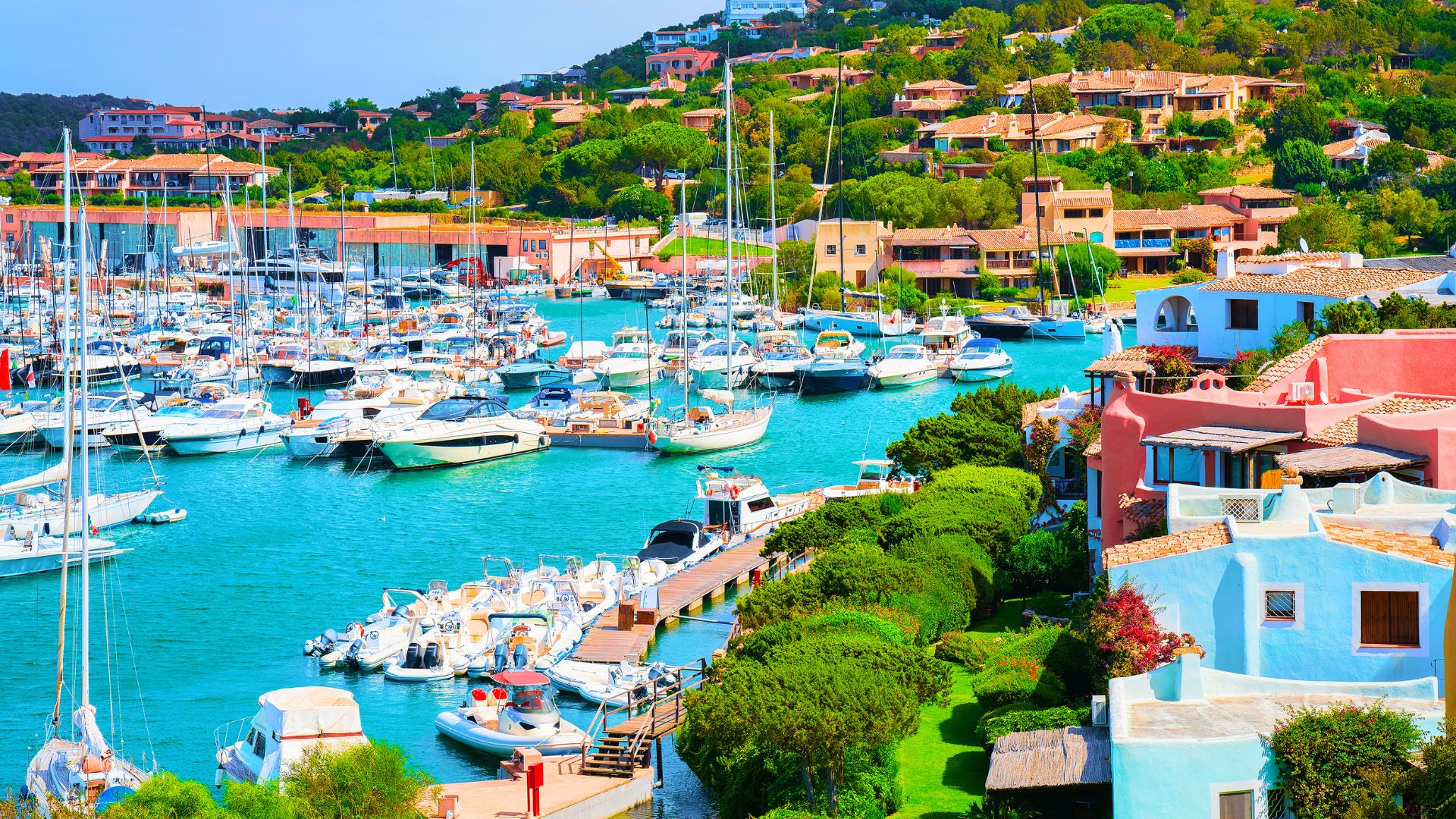 Aerial view of Porto Cervo Marina in Sardinia, Italy, filled with yachts and surrounded by colorful buildings and greenery