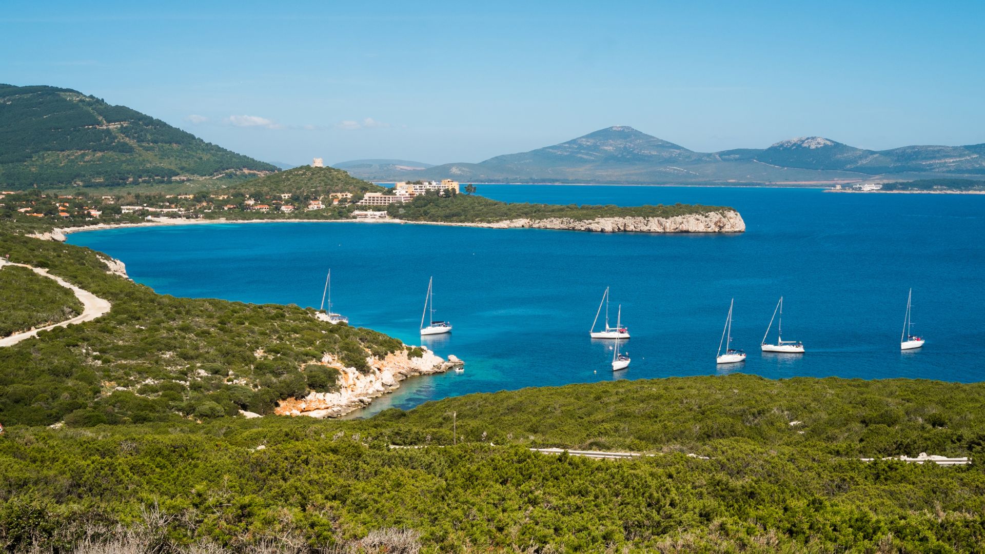 Scenic view of Porto Conte in Sardinia, featuring the coastline, boats in the bay, and surrounding hills.