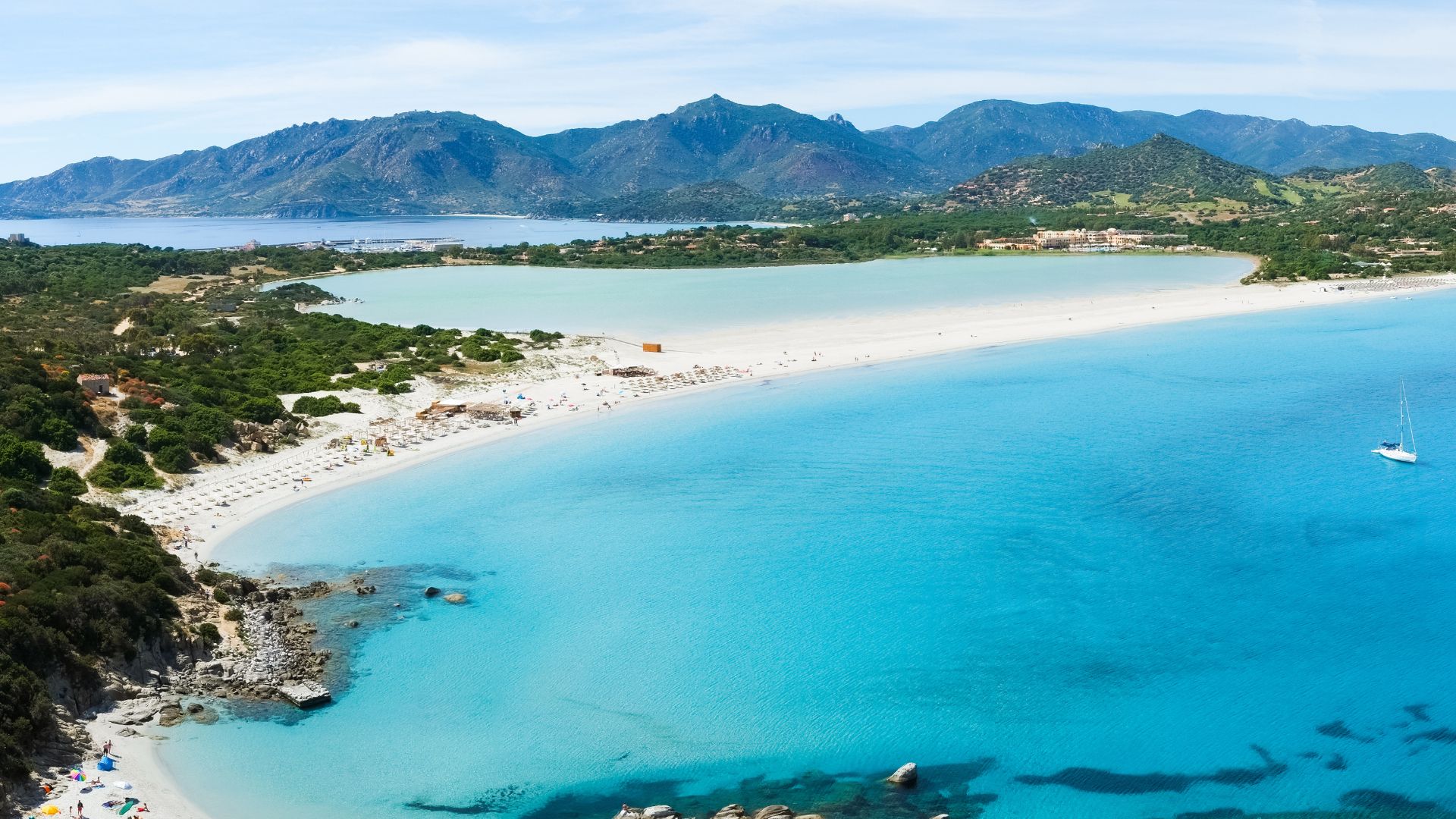 Aerial view of Porto Giunco beach in Sardinia, featuring a white sand beach, turquoise water, and surrounding green hills.
