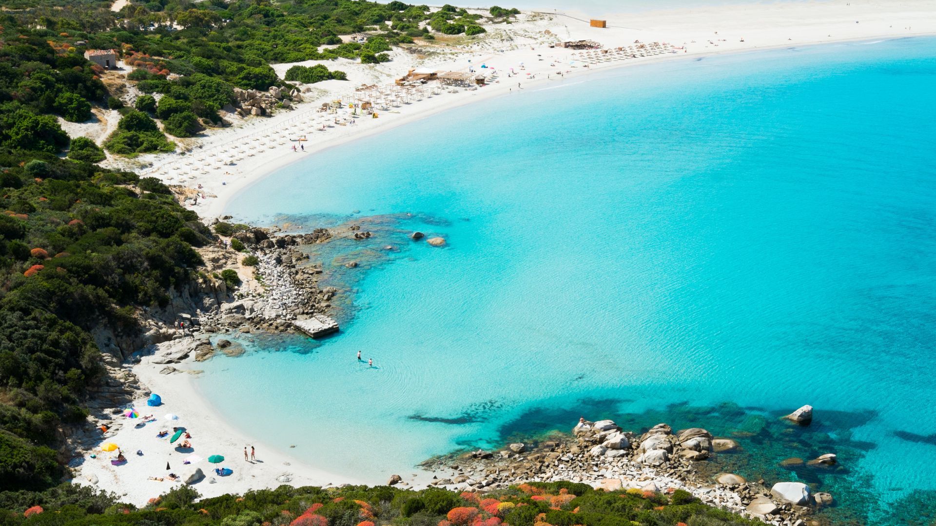 Aerial view of Porto Giunco beach in Sardinia, featuring a white sand beach, turquoise water, and surrounding green hills.